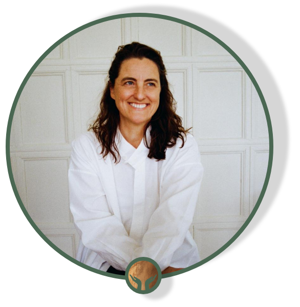 A woman with brown hair smiling, wearing a white coat, sitting in front of a white paneled wall.