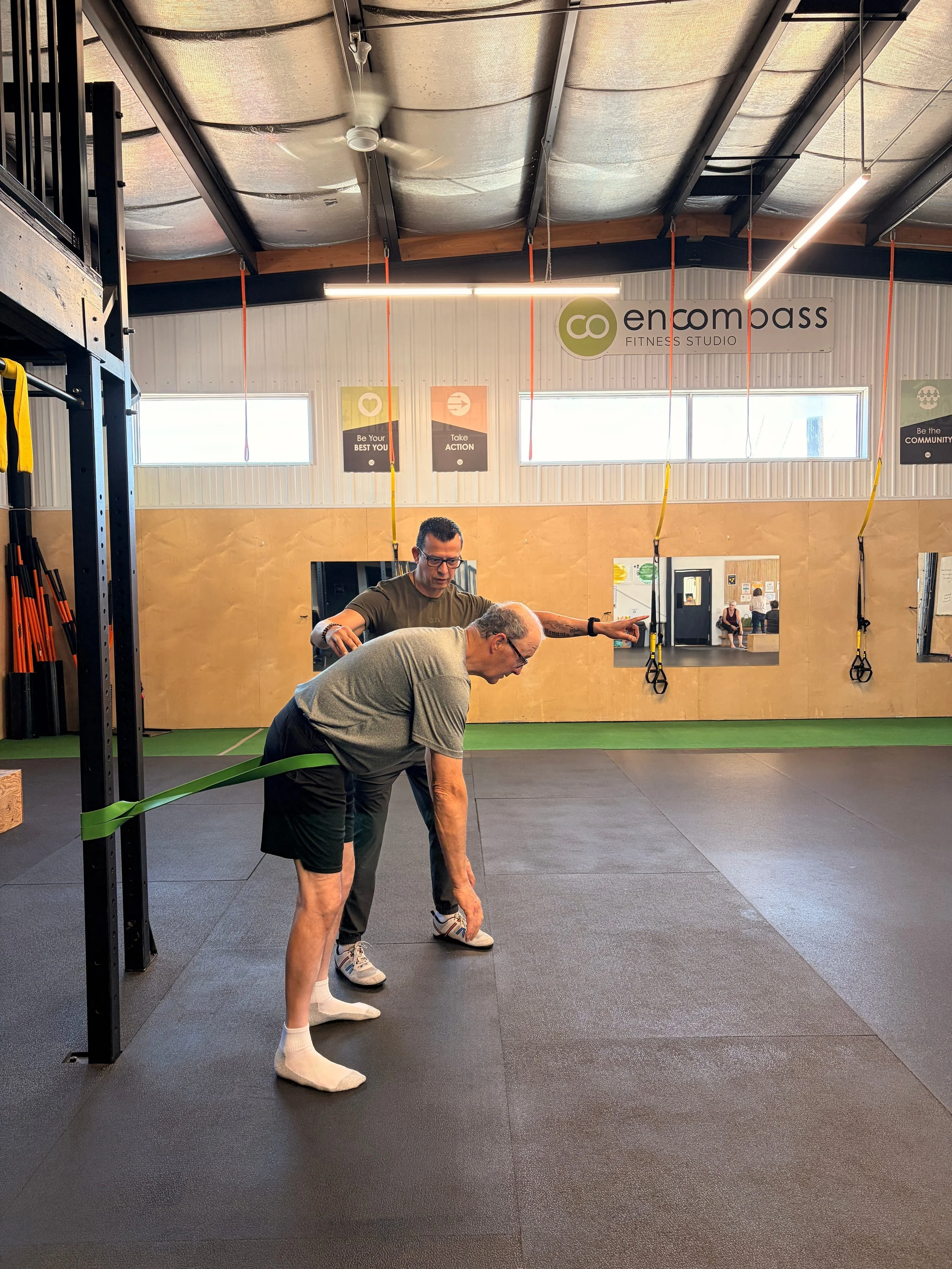 Two men stretching in a gym, with fitness equipment and motivational posters on the wall in the background.