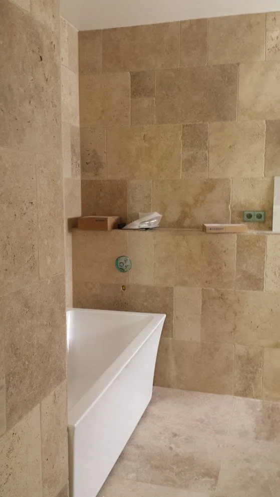 Ein Badezimmer mit beige Kacheln, eine Badewanne, eine Wand mit Steckdosen und das noch unvollständige Badezimmer. 
