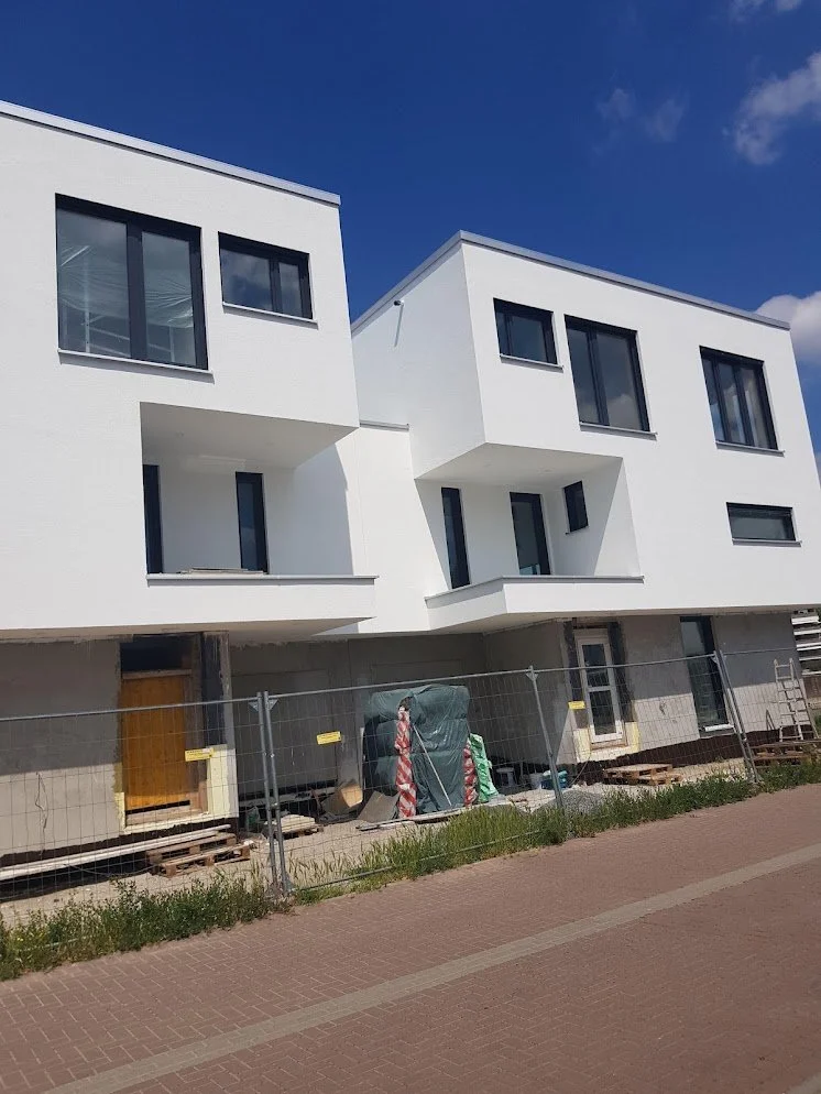 Neues weißes Mehrfamilienhaus im Bau mit sichtbarer Baustelle und Zaun davor.