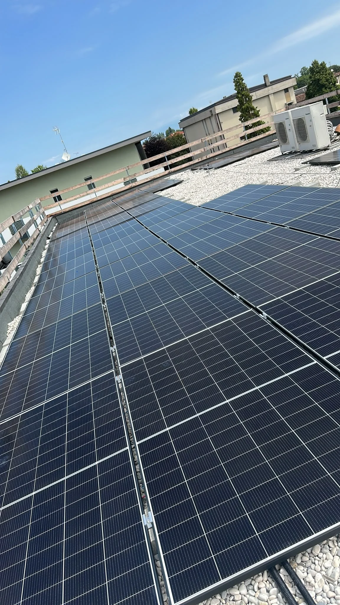 Dach mit Solarpanelen auf einem Flachdach, im Hintergrund Bäume und Gebäude, blauer Himmel.
