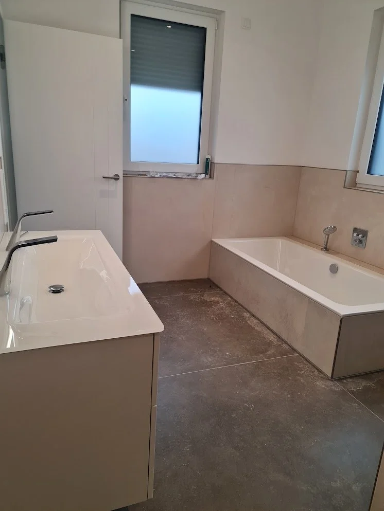 Ein Badezimmer mit einem Waschtisch, einer Badewanne, Fenstern und beige Wandfliesen.