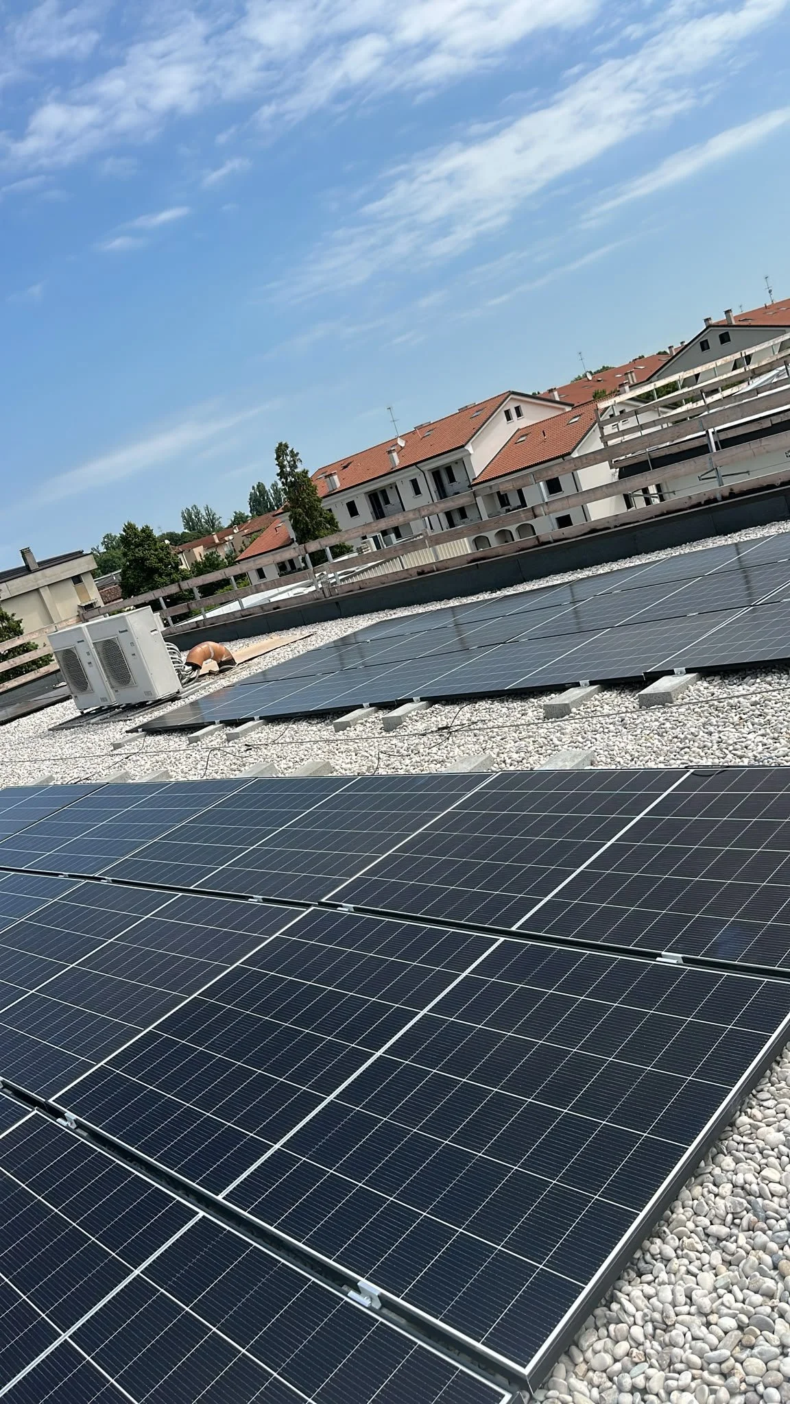 Solarmodule auf einem Dach, mit Wohnhäusern im Hintergrund und einem blauen Himmel mit wenigen Wolken.