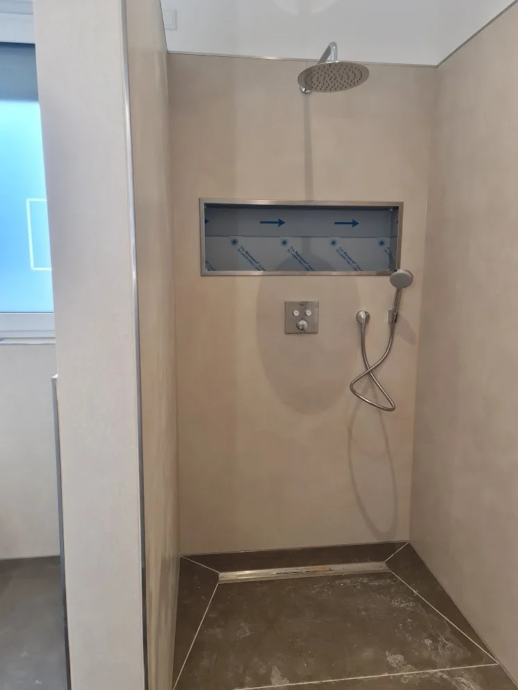 Ein barrierefreies Duschbad mit einem Regenwaldduschkopf, Handbrause, Wasserschalter und ein kleines Fenster mit einem Pfeildiagramm.