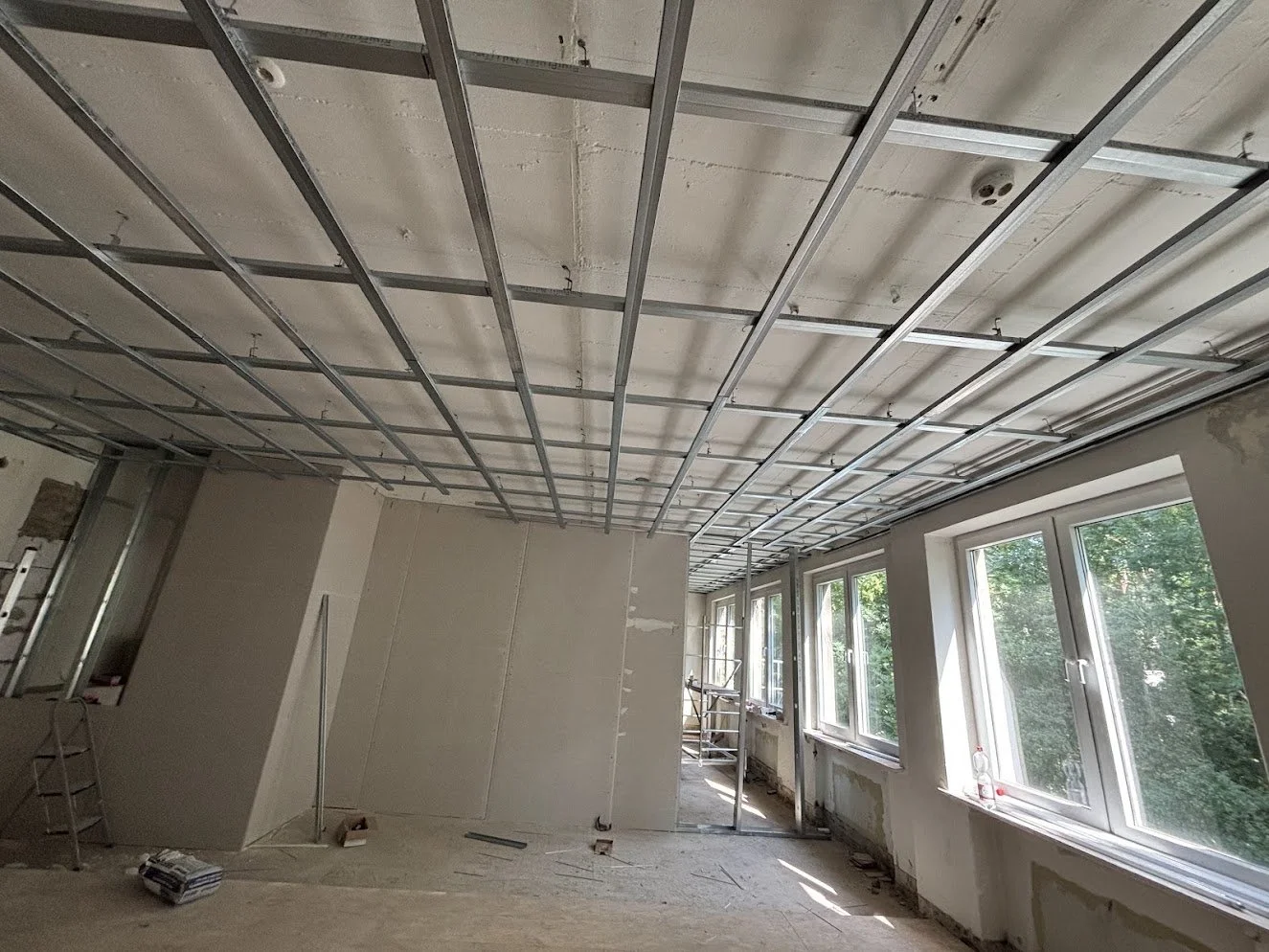 Innenraum eines Hauses unter Renovierung mit Metallrahmen an der Decke und großen Fenstern