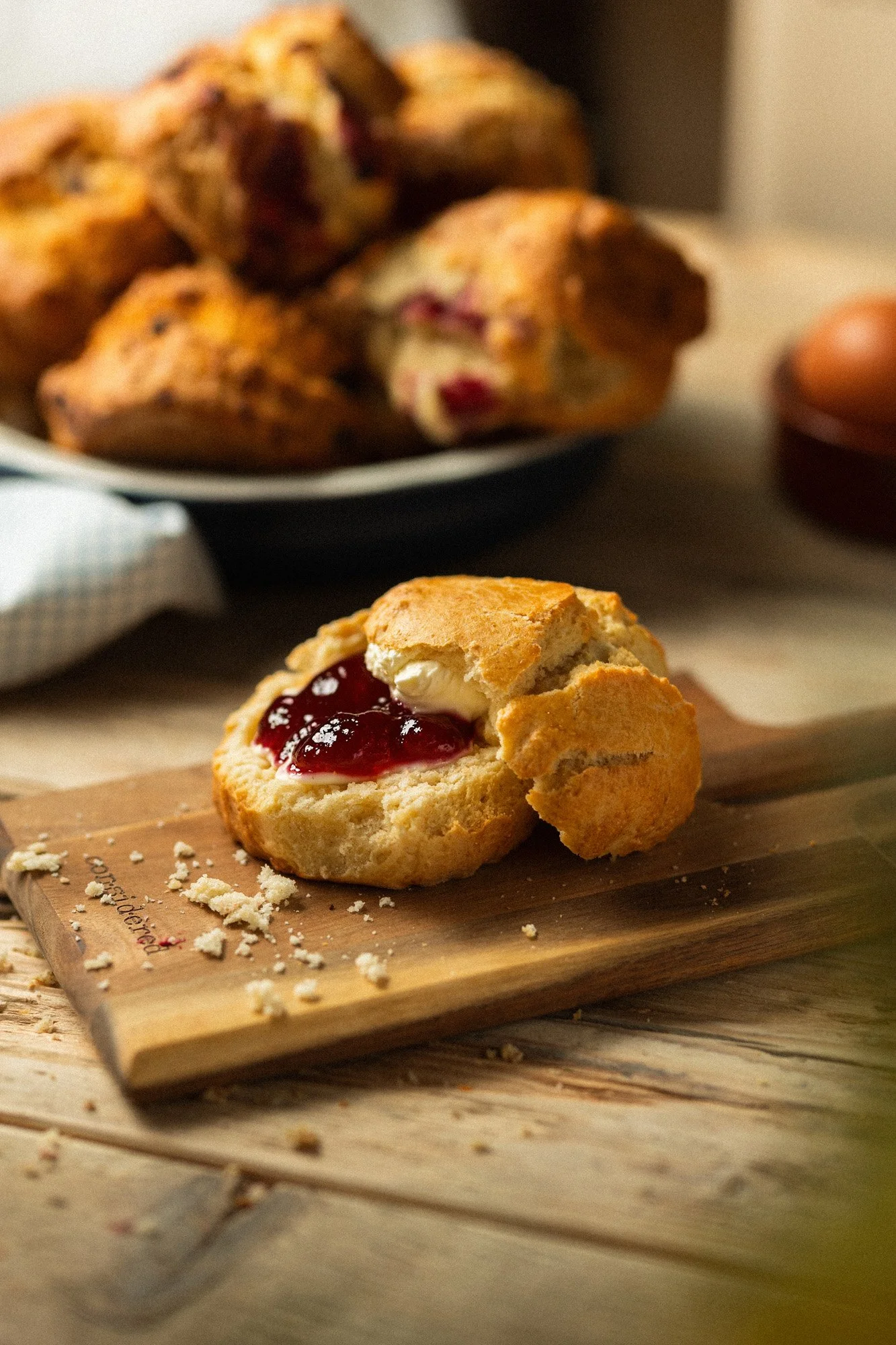 Freshly baked scone with butter and raspberry jam served on a wooden board at O'Keeffe's Bakery, with homemade fruit scones in the background.