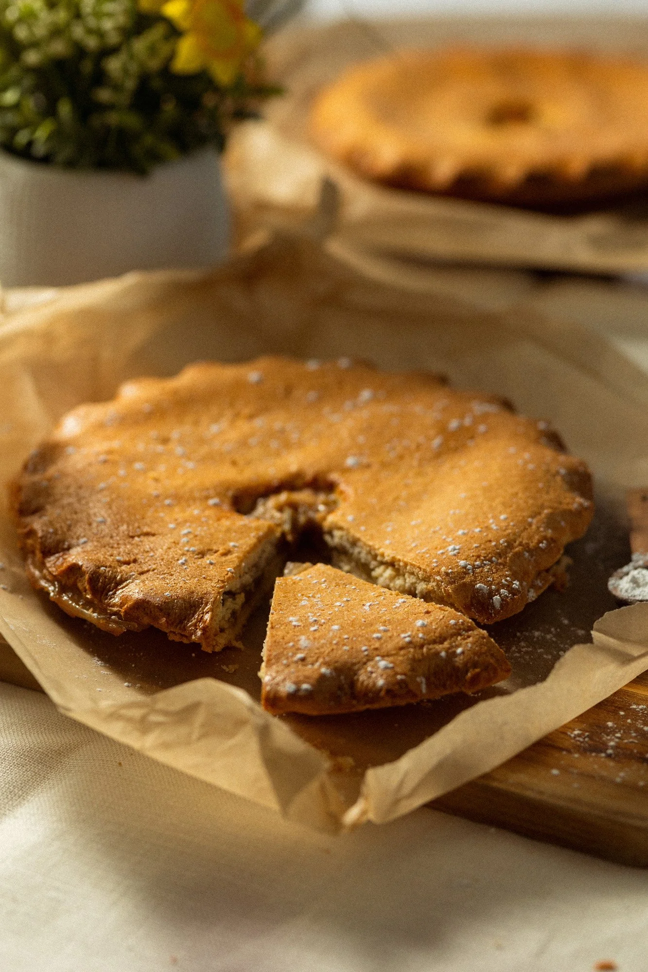 Freshly baked traditional tart with a slice removed, lightly dusted with icing sugar and served on baking paper.