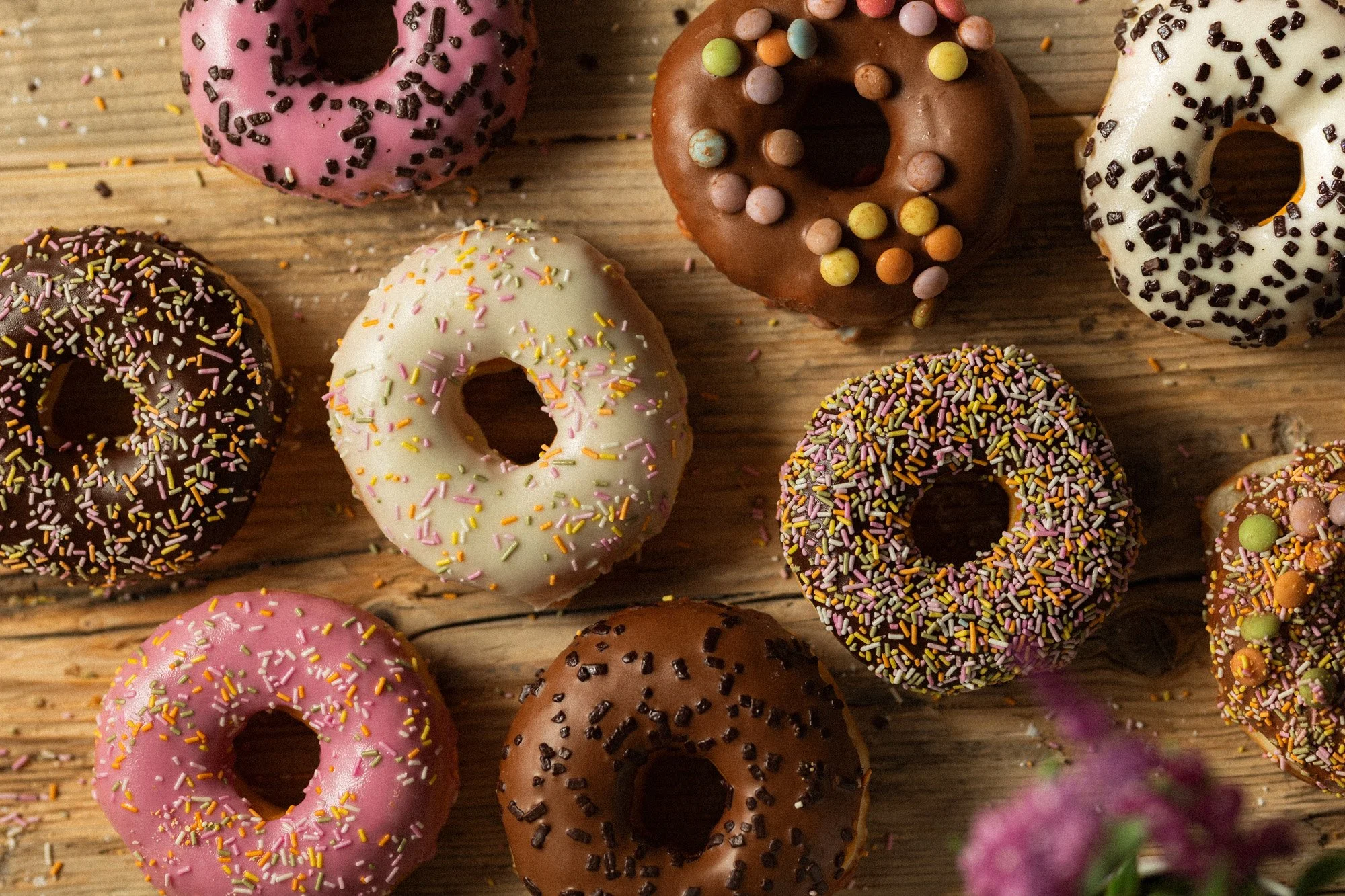 Selection of colourful iced doughnuts with chocolate, vanilla and strawberry glazes topped with sprinkles.