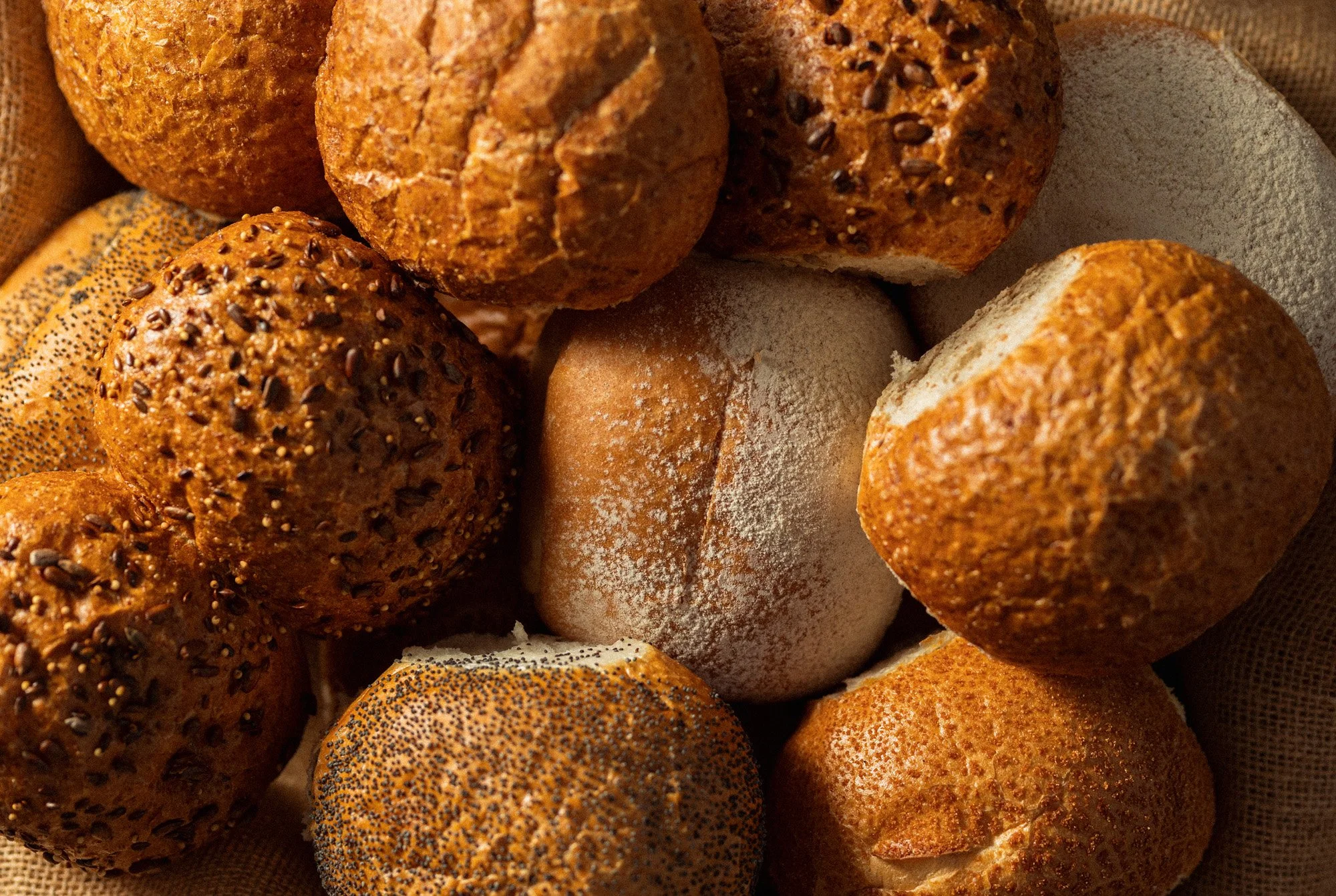 Selection of freshly baked white, seeded and poppy seed bread rolls stacked together in a basket.