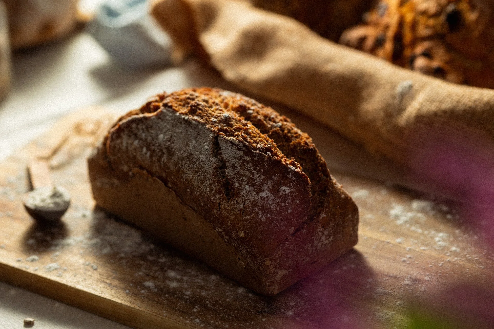 Dark, flour-dusted loaf of soda bread on a wooden board, lit with strong side light