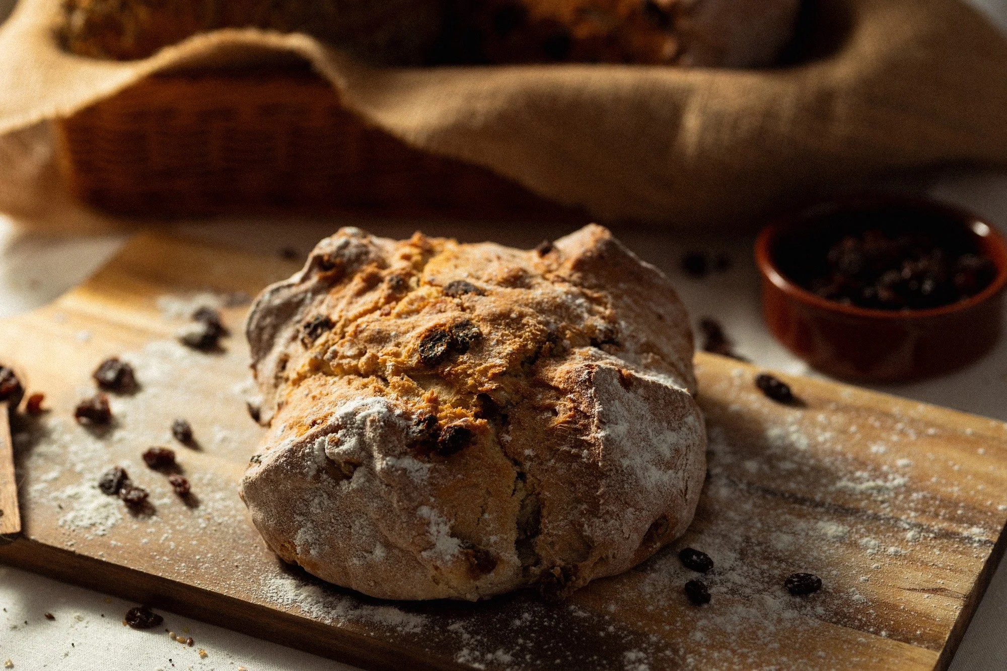 Traditional Irish fruit soda bread dusted with flour and baked with raisins, displayed on a wooden board.