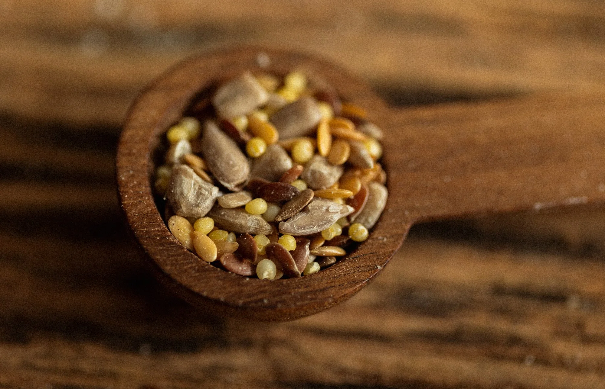 Mixed sunflower, sesame and flax seeds in a small wooden scoop