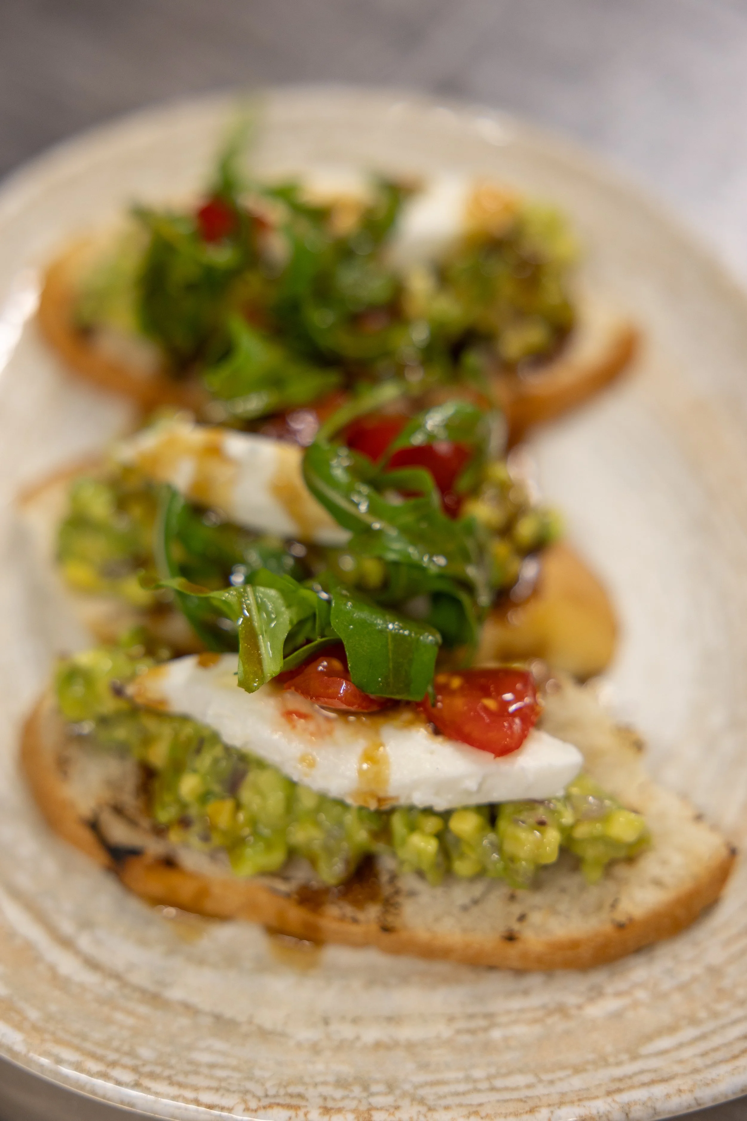 Close-up of an open-faced bread sandwich topped with green arugula, cherry tomatoes, and melted cheese.