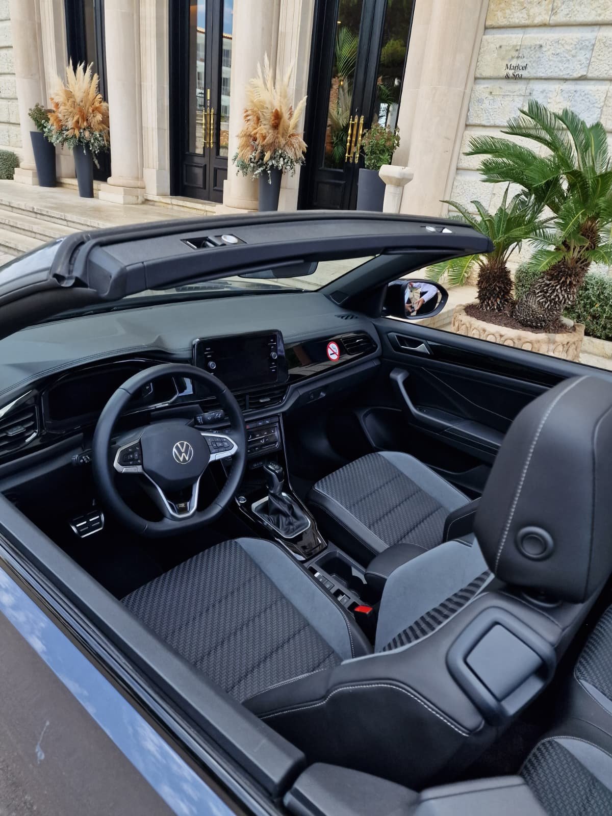 Interior of a Volkswagen convertible car parked outside a building with potted plants and floral arrangements.
