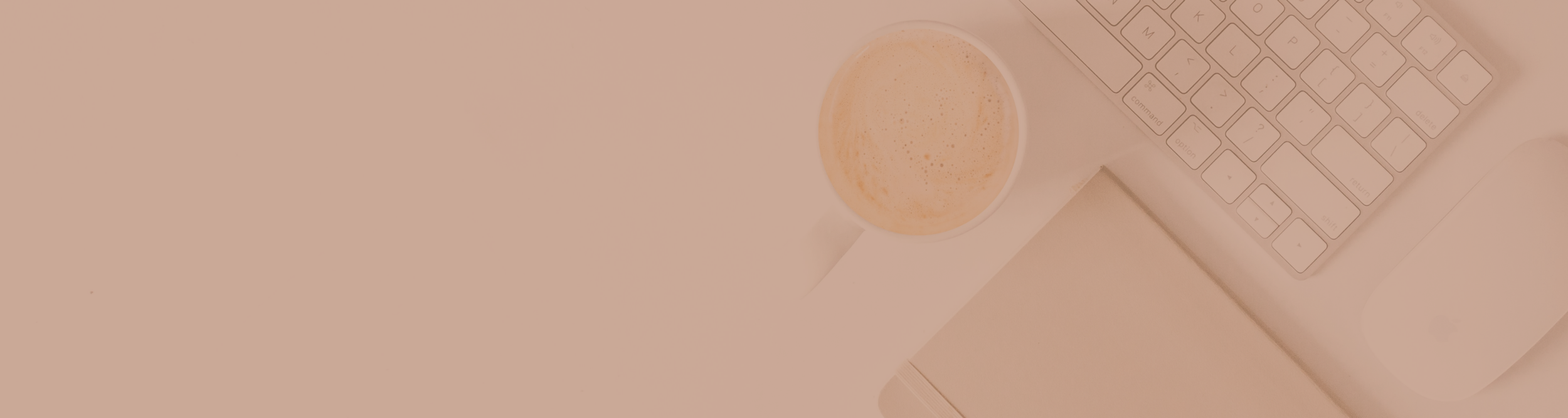 A white computer keyboard, a cup of coffee with foam, and a white notebook on a desk with a beige background.