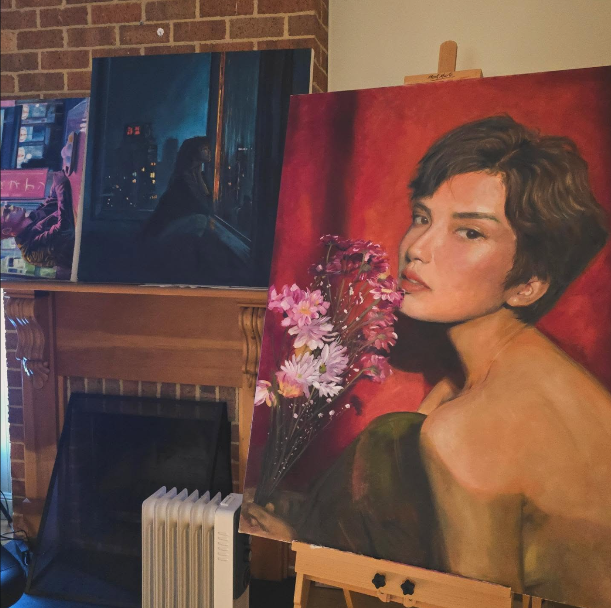 An art gallery display with several paintings, including a portrait of a woman holding pink flowers, a cityscape at night, and a person looking out a window.