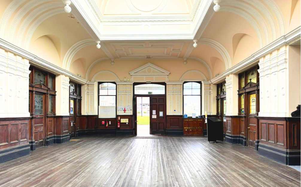 An empty historic room with high, vaulted ceiling, large windows, and dark wooden paneling on the walls.