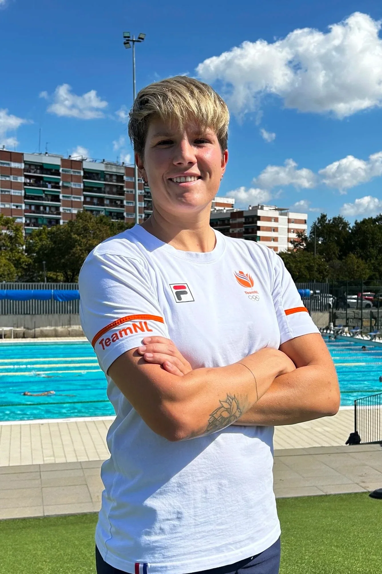 Laura Aarts standing beside an outdoor swimming pool in a TeamNL shirt.