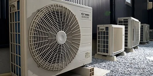 Multiple outdoor air conditioning units on a gravel surface.