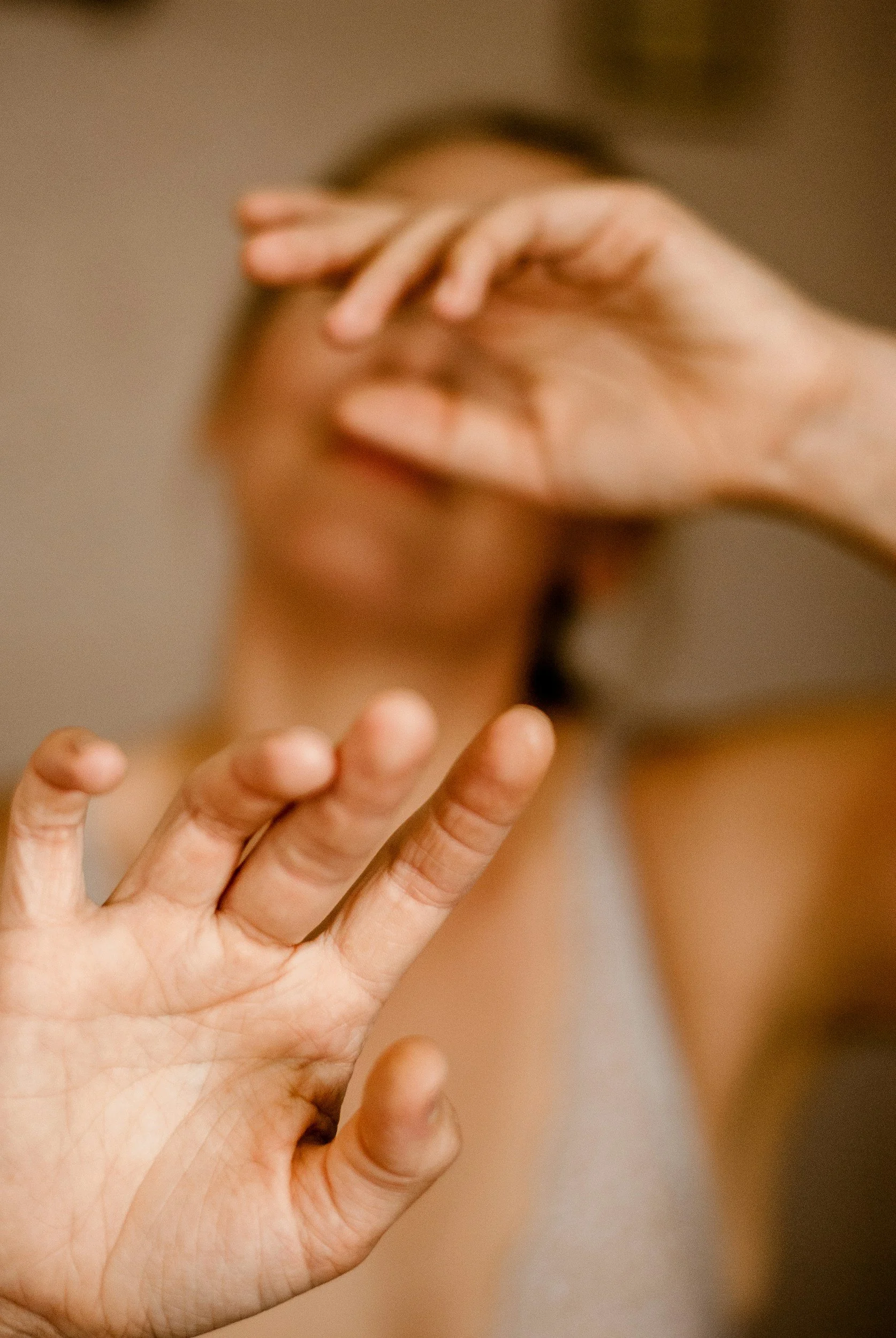 Close-up of a person's hand with fingers slightly spread, held in front of their face, which is blurred in the background.