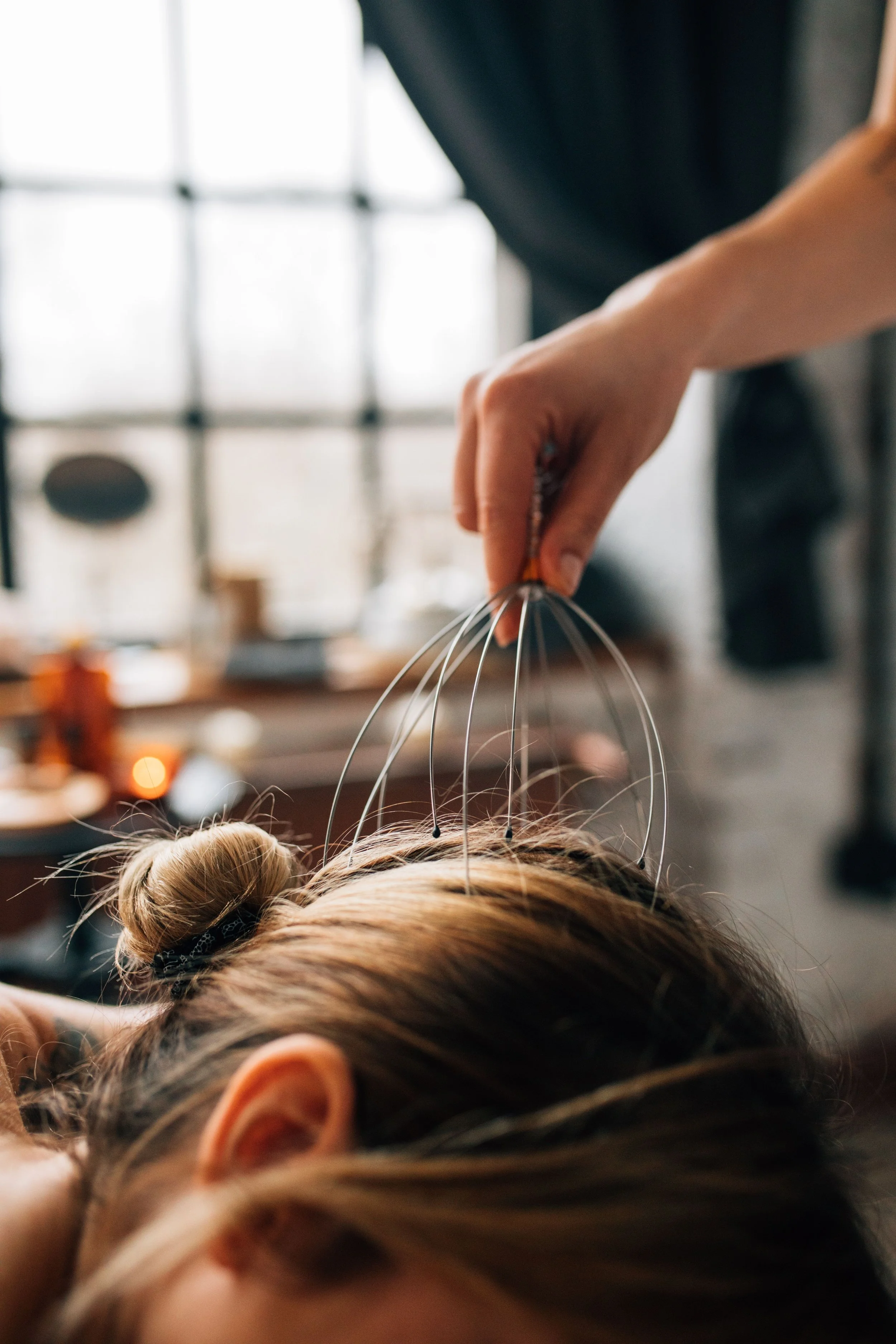 A person with blonde hair in a bun lying down, receiving a scalp treatment with multiple small wires attached to their head, in a well-lit room.
