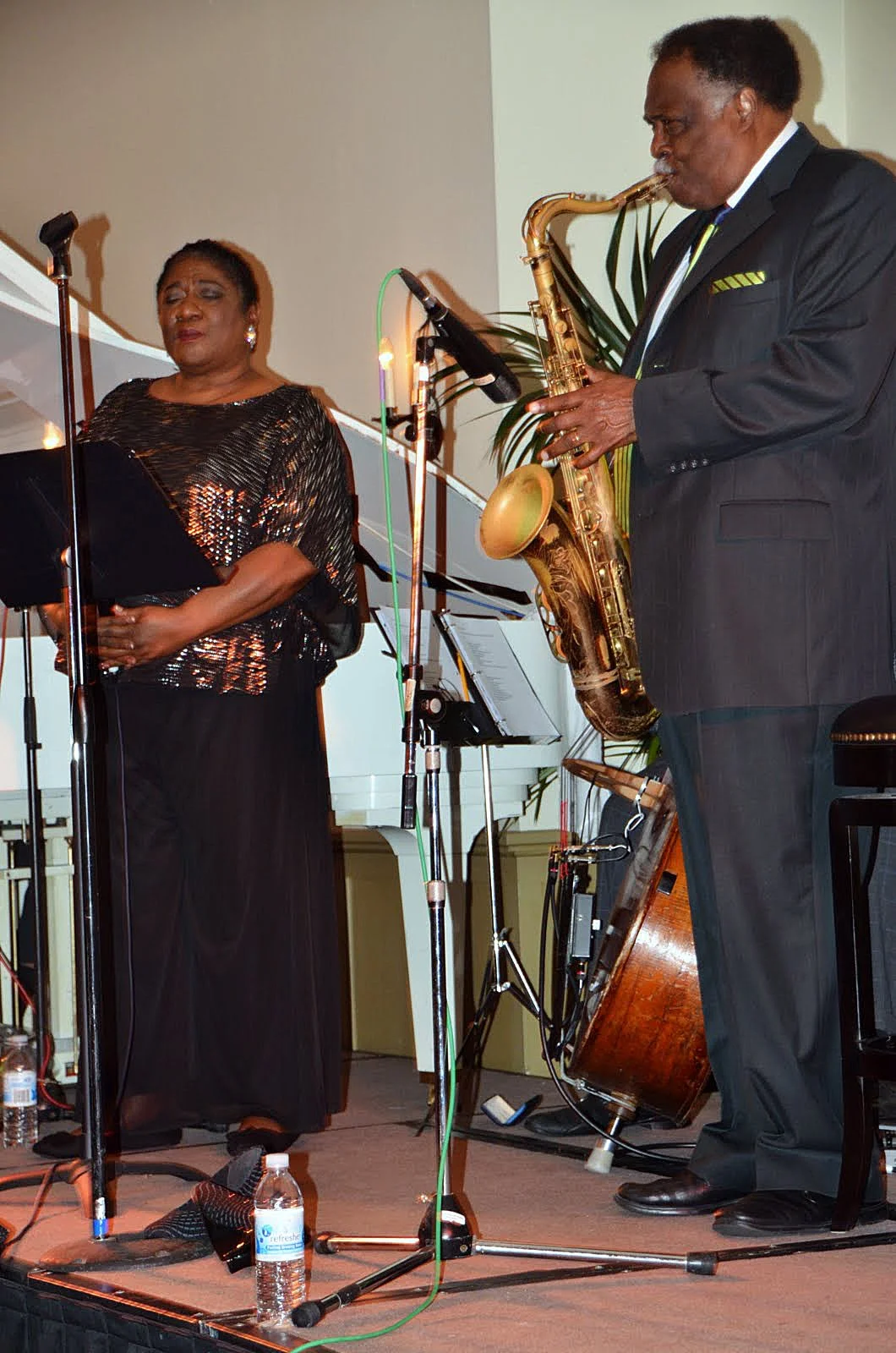 A woman singing and a man playing a saxophone on stage during a musical performance.