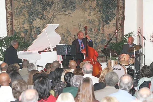 Jazz musicians performing on stage with a pianist, double bassist, and drummer in front of an audience.