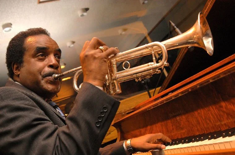 Man playing trumpet while sitting at a piano.