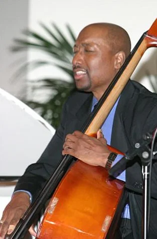 Man playing the piano while holding a double bass.