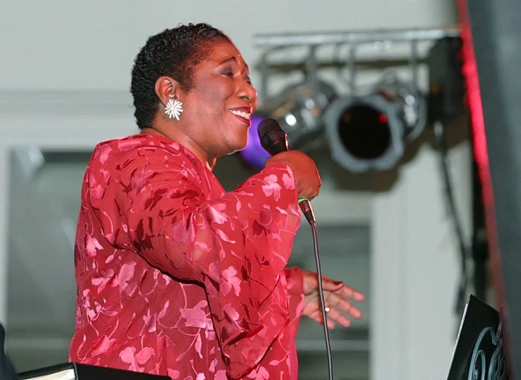 African American woman singing into a microphone at an indoor event.