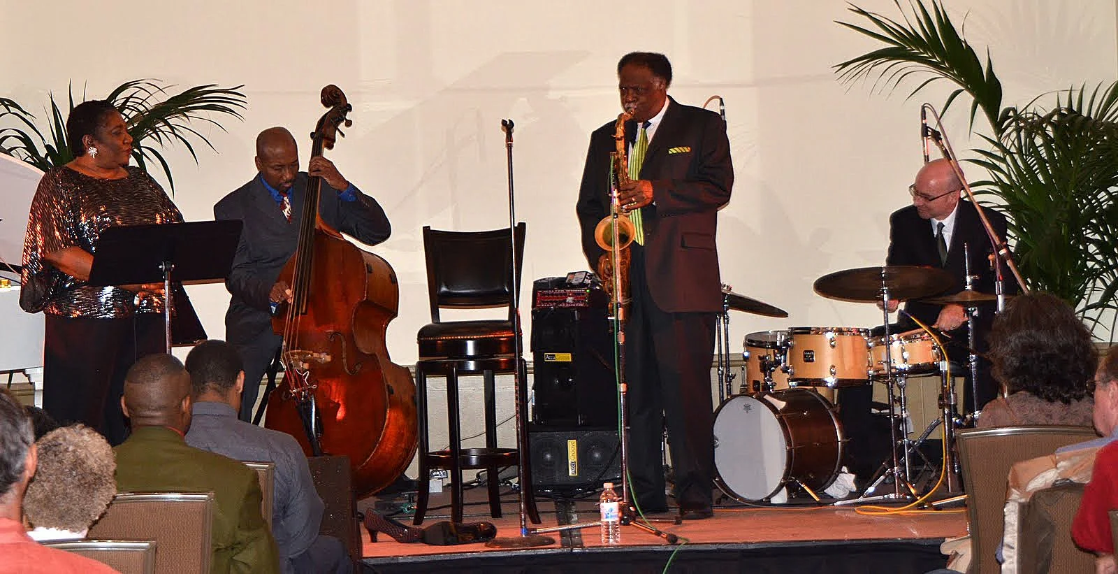 Jazz band performing on stage with four musicians playing instruments and audience watching.