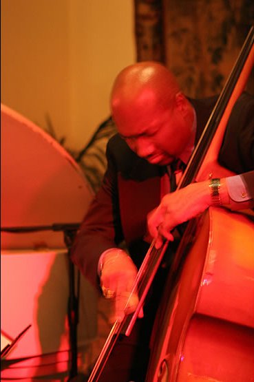 Man playing double bass with a focused expression in a warmly lit room.