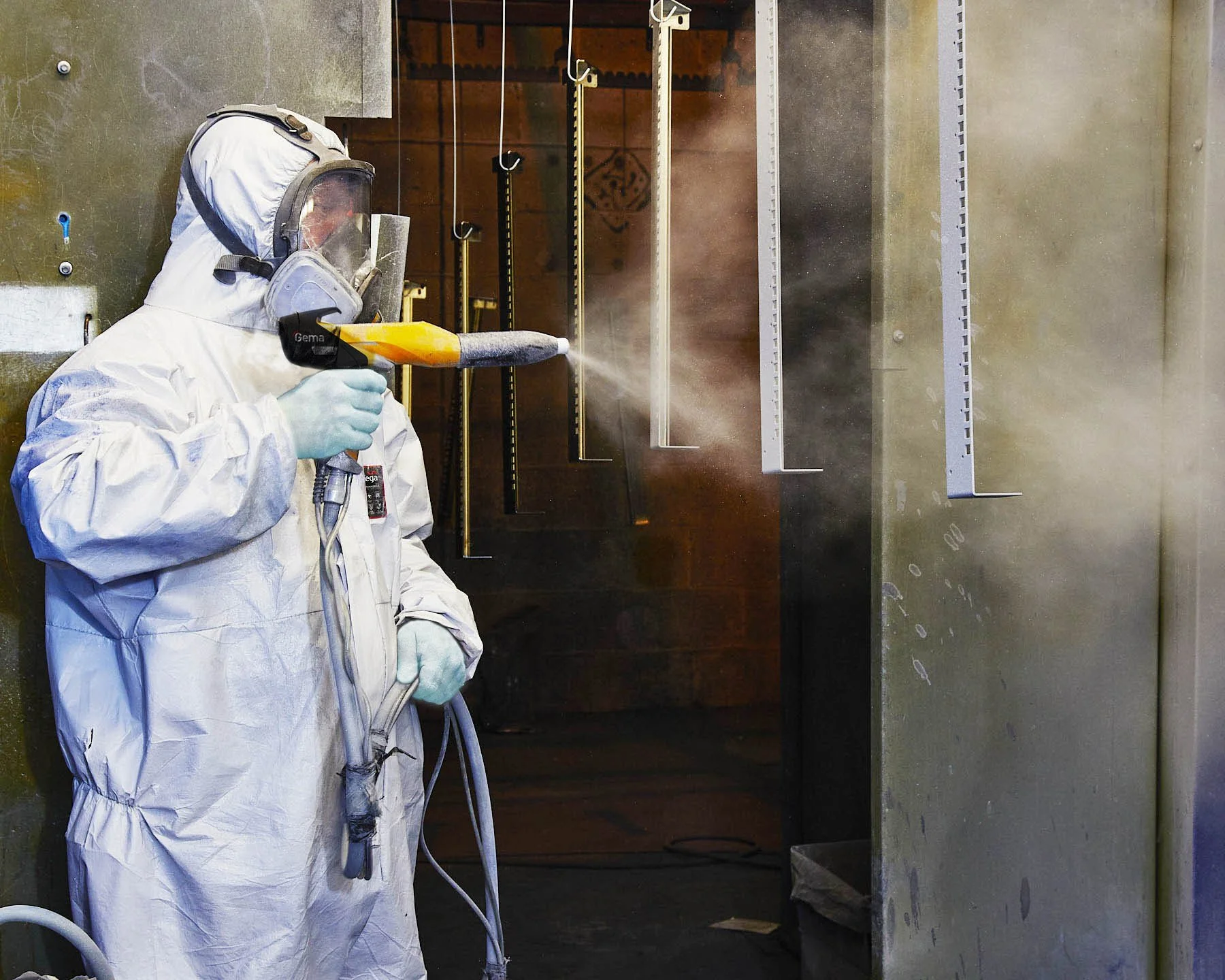 Person in protective suit, mask, and gloves using a handheld sprayer inside an industrial or laboratory environment.