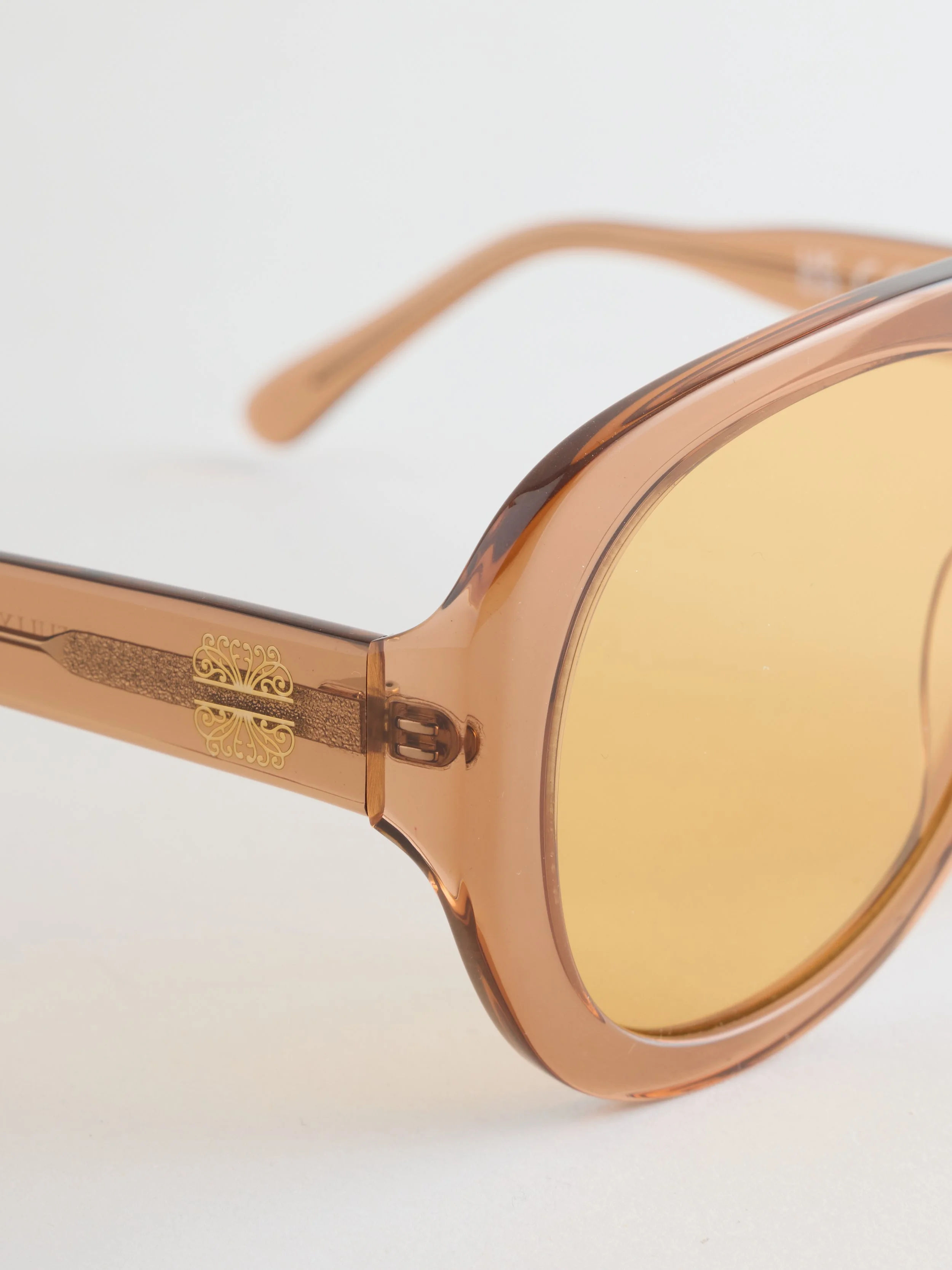Close-up of a pair of designer sunglasses with a peach-colored frame and yellow tinted lenses, placed on a white surface.