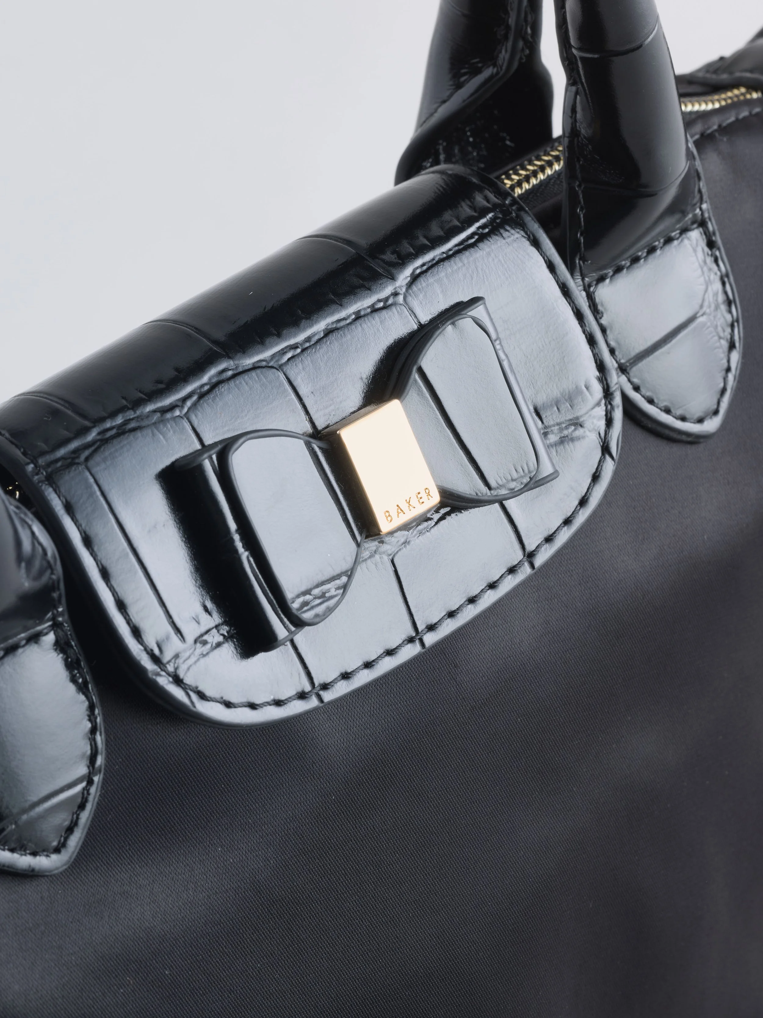 Close-up of a black leather handbag with gold zipper and handle, on a black surface.