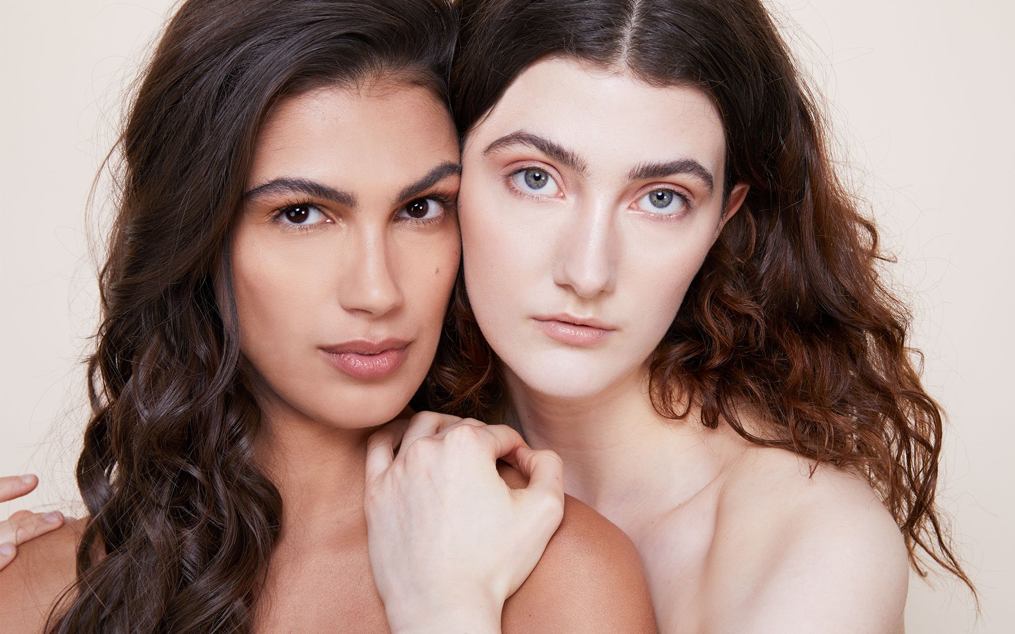 Two women with different hair colors and styles pose closely together against a plain background.