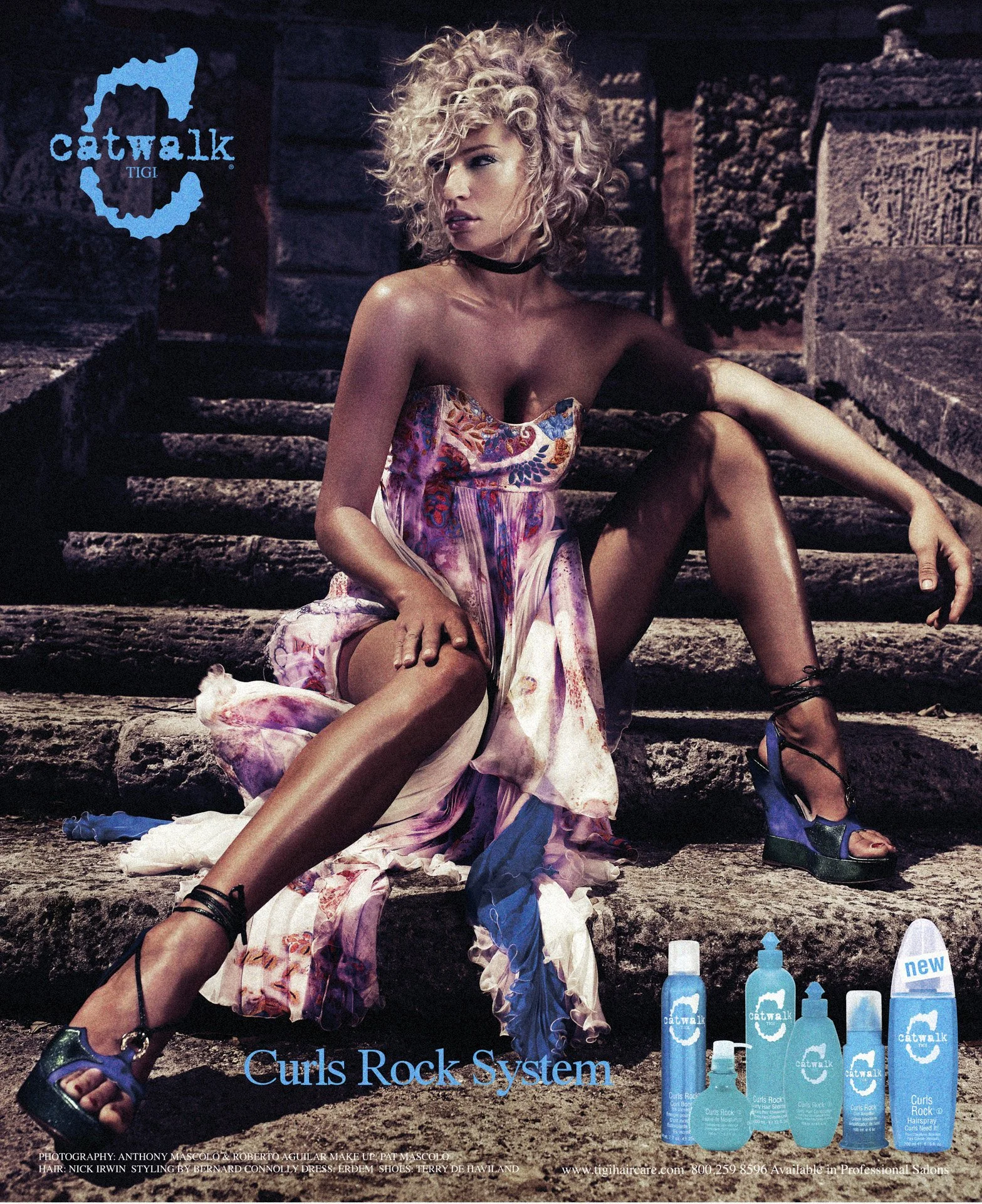 A woman with curly blonde hair sitting on stone steps, wearing a colorful strapless dress, black high heel sandals, with seen hair products in front, and a blue logo with a map of California and the words 'catwalk TIGI' in the top left corner.