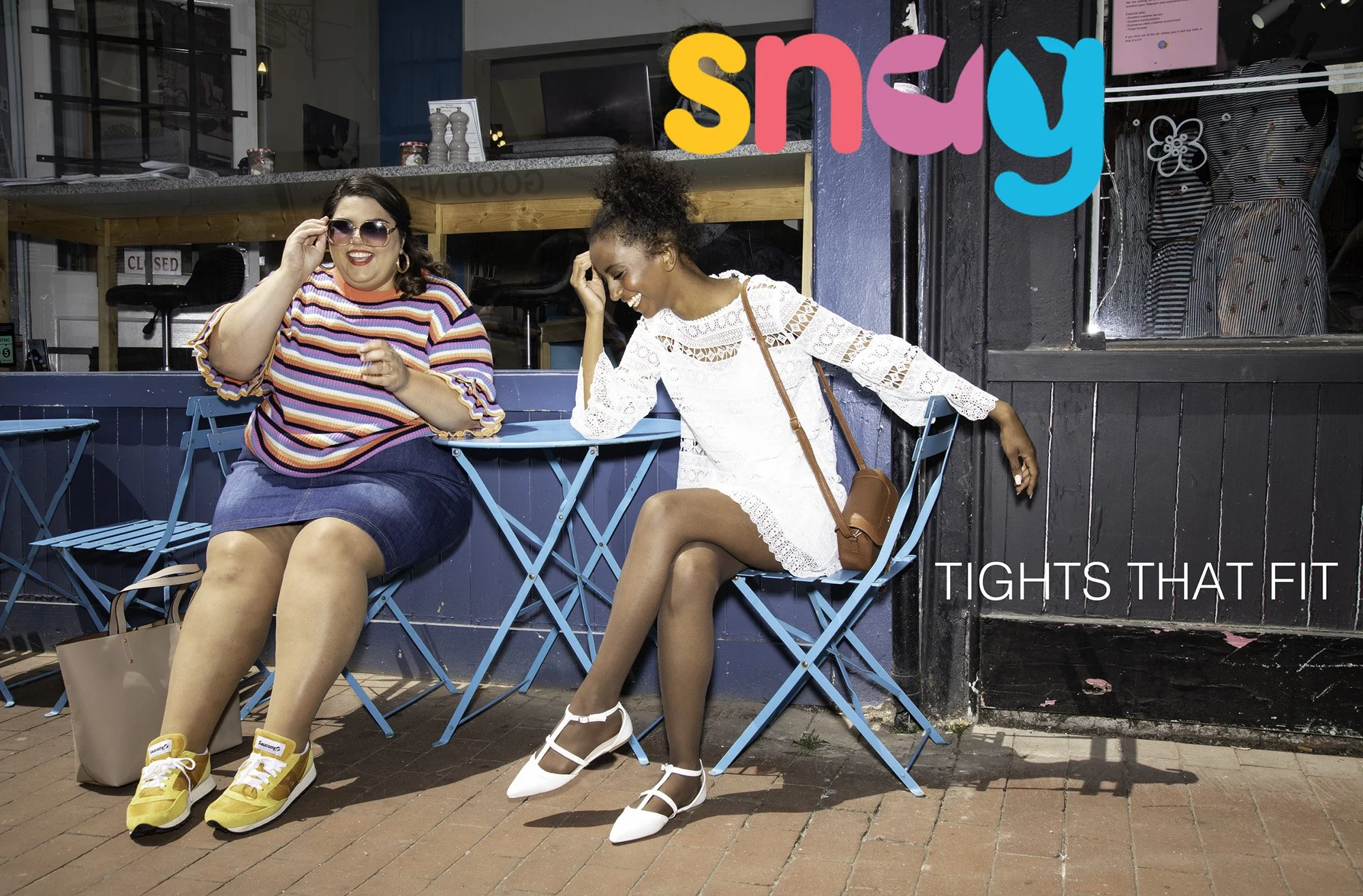Two women sitting outdoors at a cafe, both wearing colorful and white tights that fit well. One woman is adjusting her sunglasses and wearing a striped top, yellow shoes, and has a beige bag on the ground beside her. The other woman is in a white lac