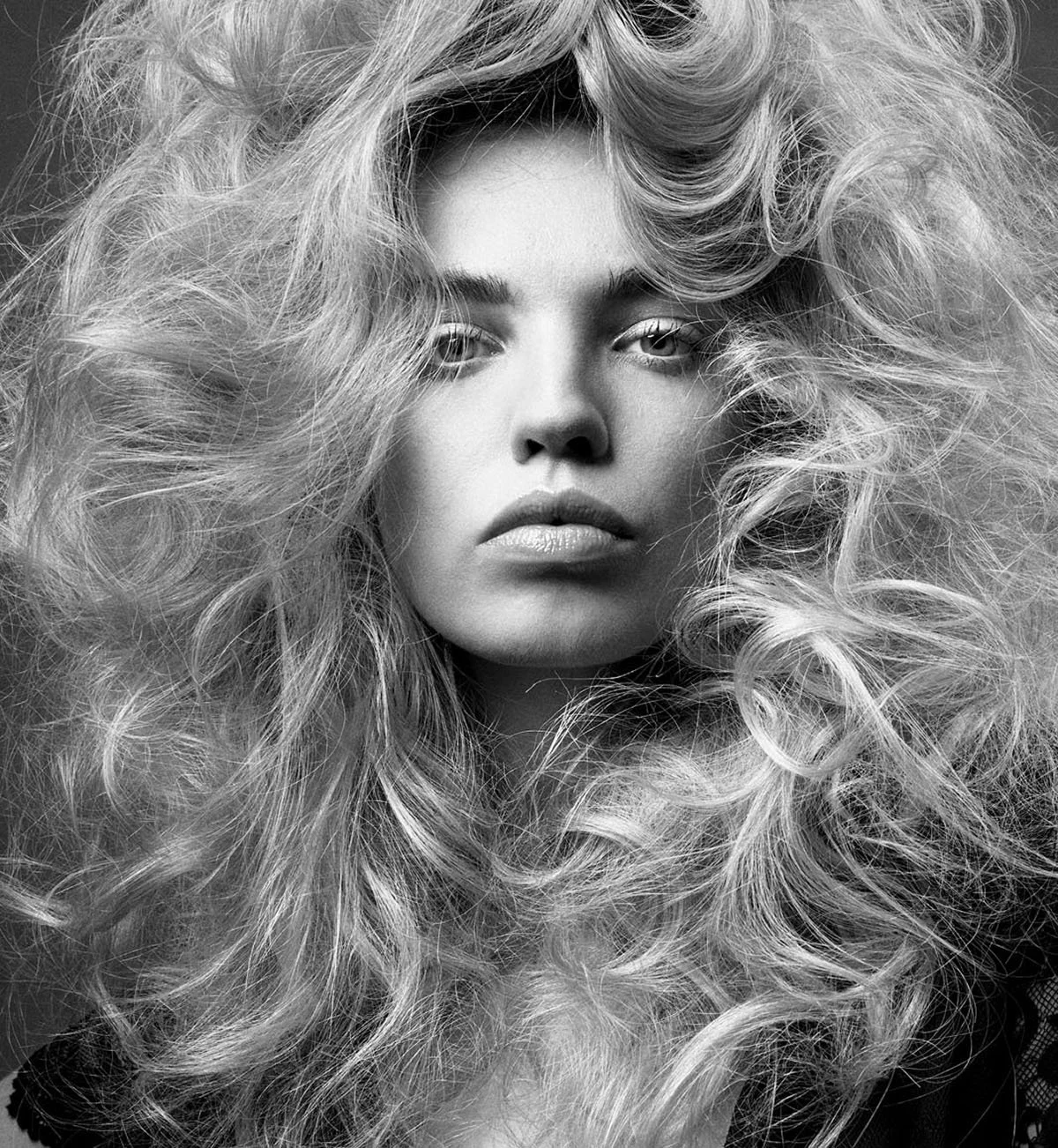 Black and white close-up photo of a woman with voluminous, curly hair partially covering her face and intense expression.