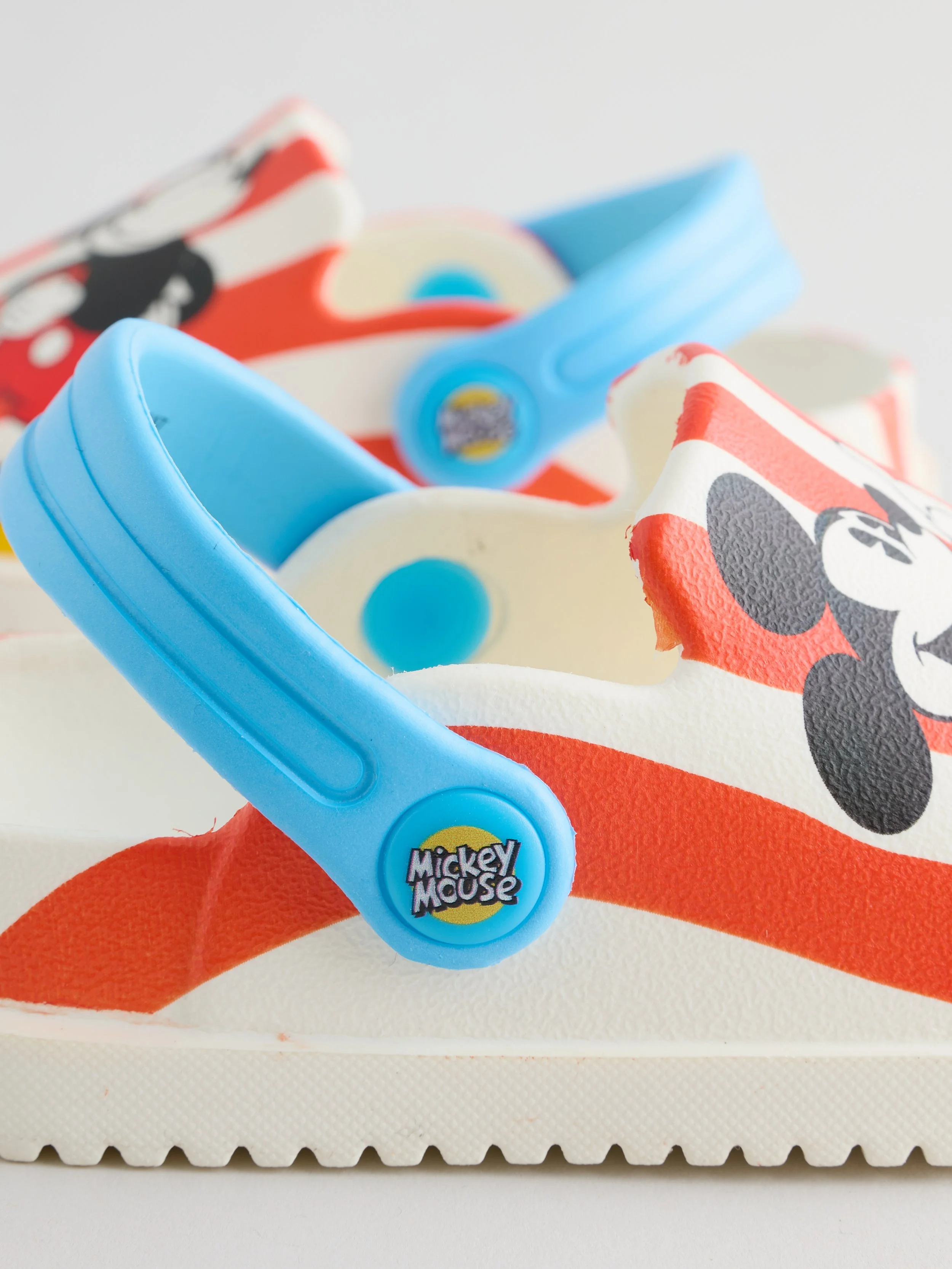 Close-up of a Mickey Mouse-themed cake with colorful fondant decorations and a plastic knife with a Mickey Mouse logo.