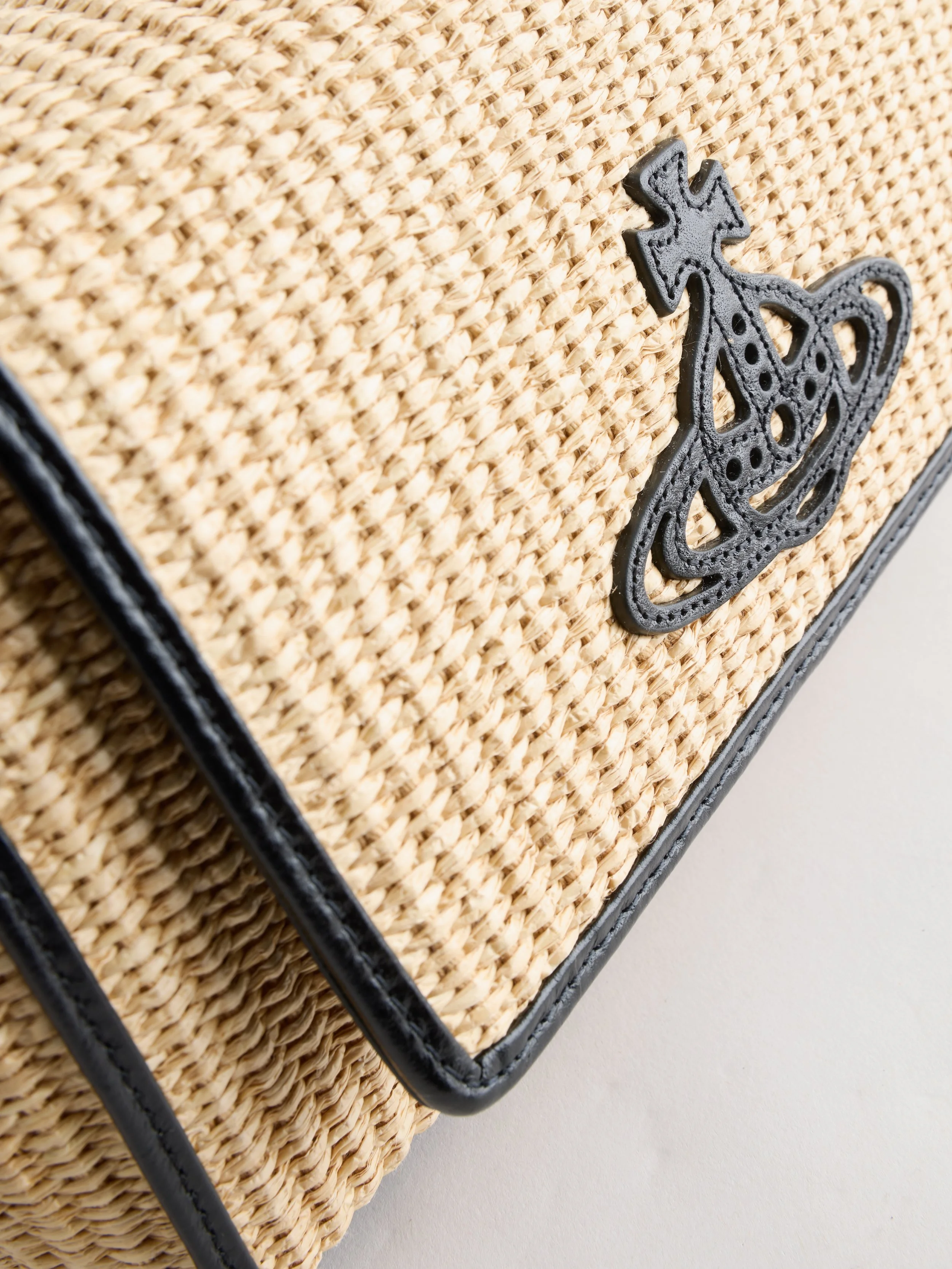 Close-up of a woven straw handbag with a decorative black leather butterfly appliqué.