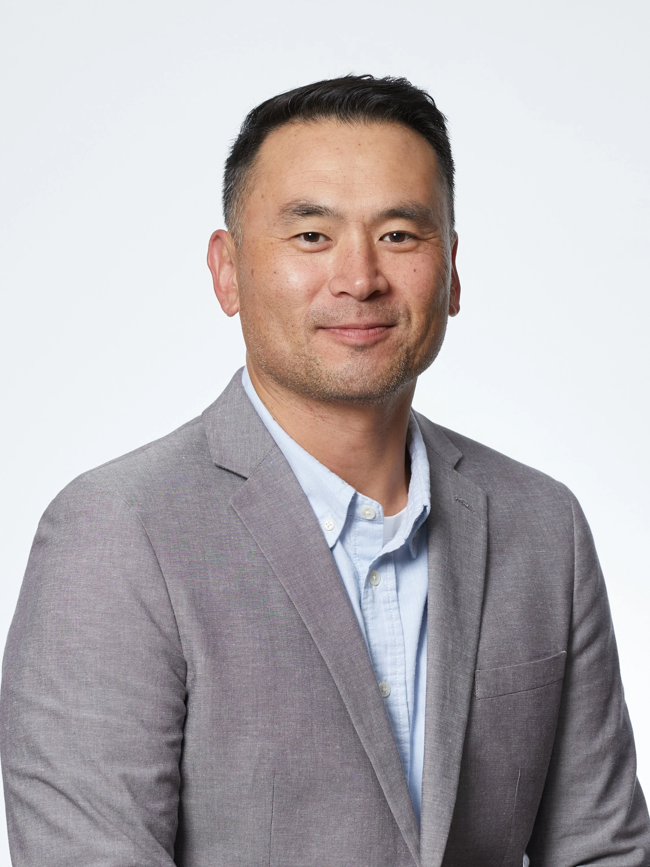 Portrait of an Asian man wearing a light gray suit and light blue shirt against a plain white background.
