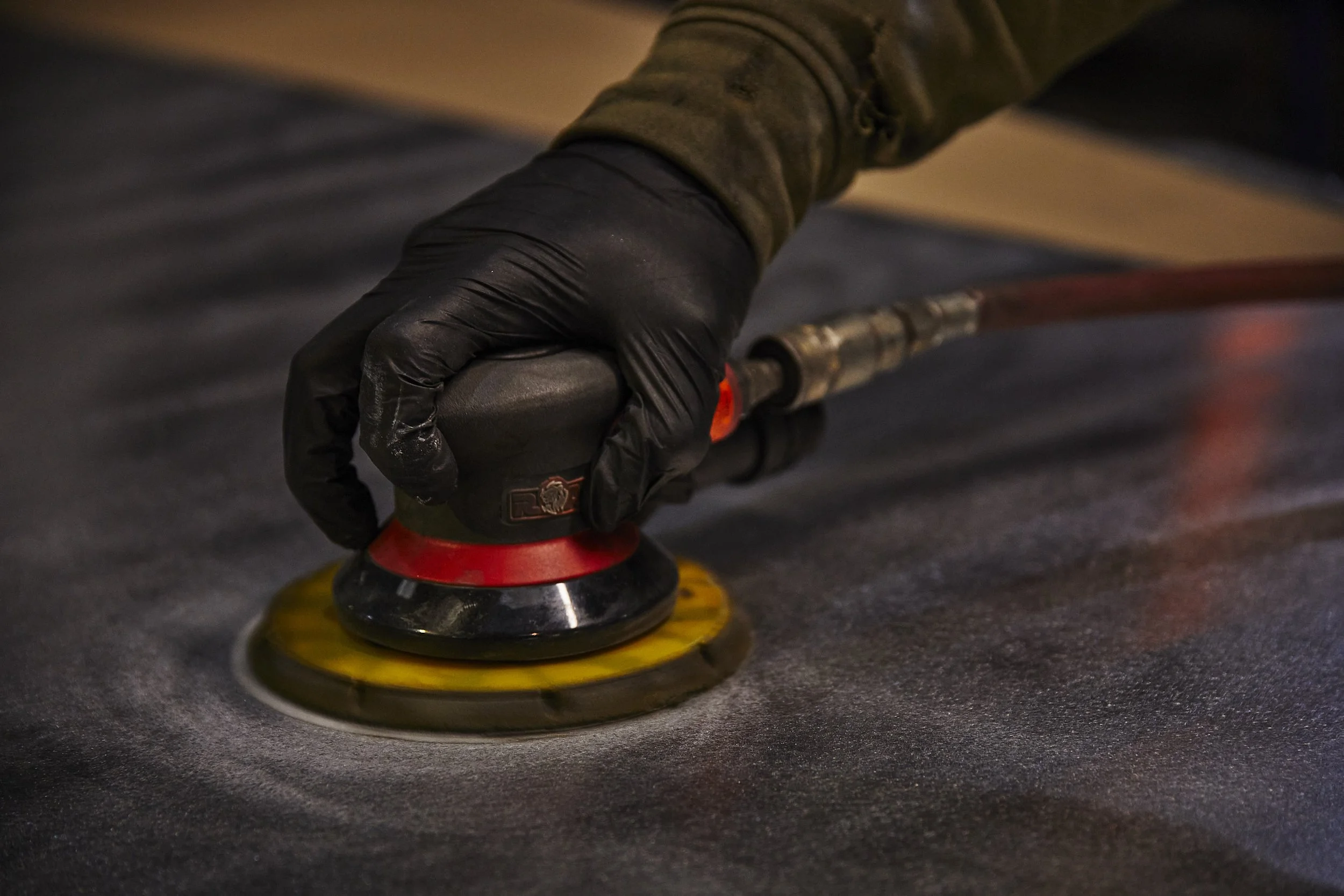 Close-up of a hand wearing a black glove using a polishing or buffing machine on a dark surface.