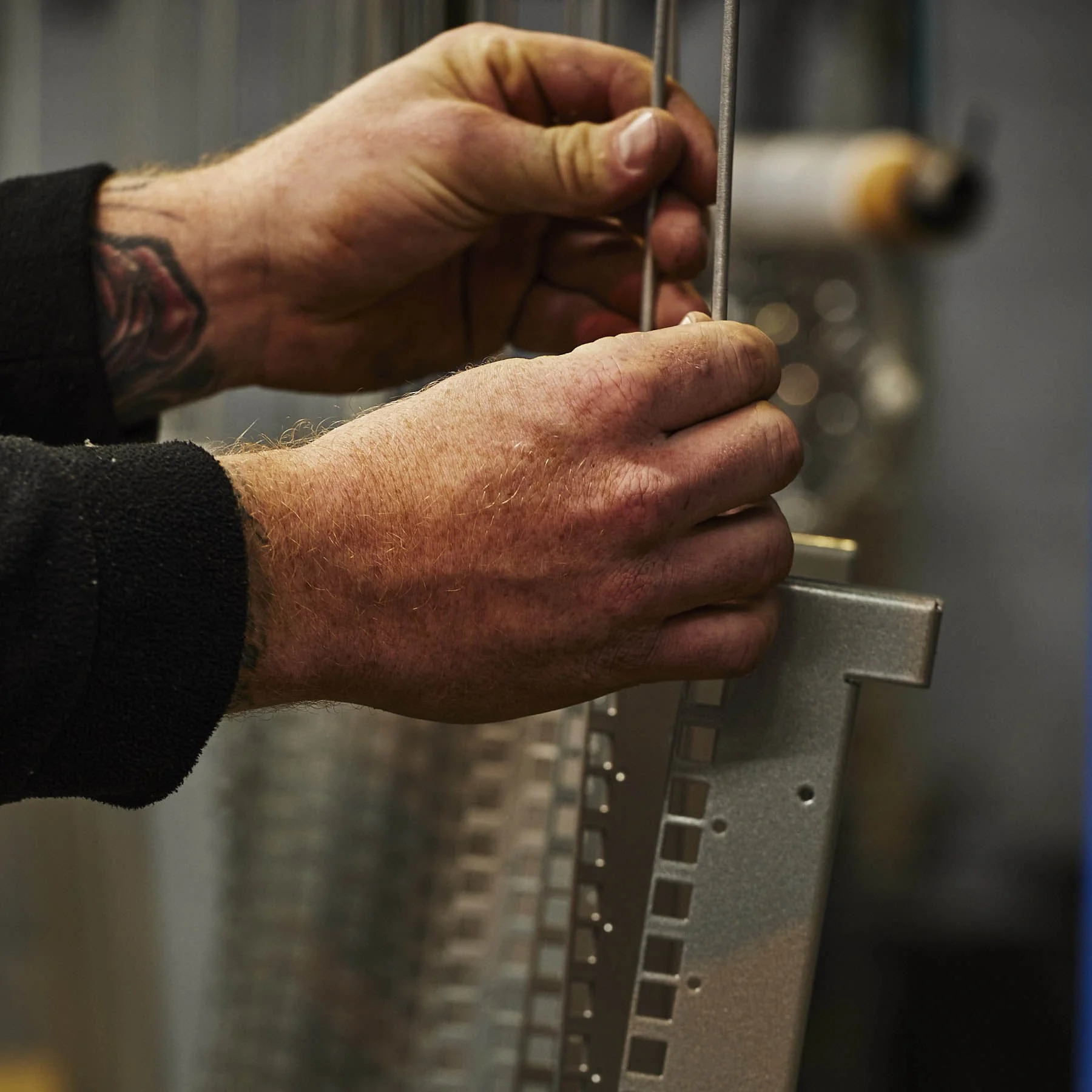 A person's hand holding a file or a tool, with some tattoo visible on the wrist, working on an electronic or mechanical device with a metallic surface.