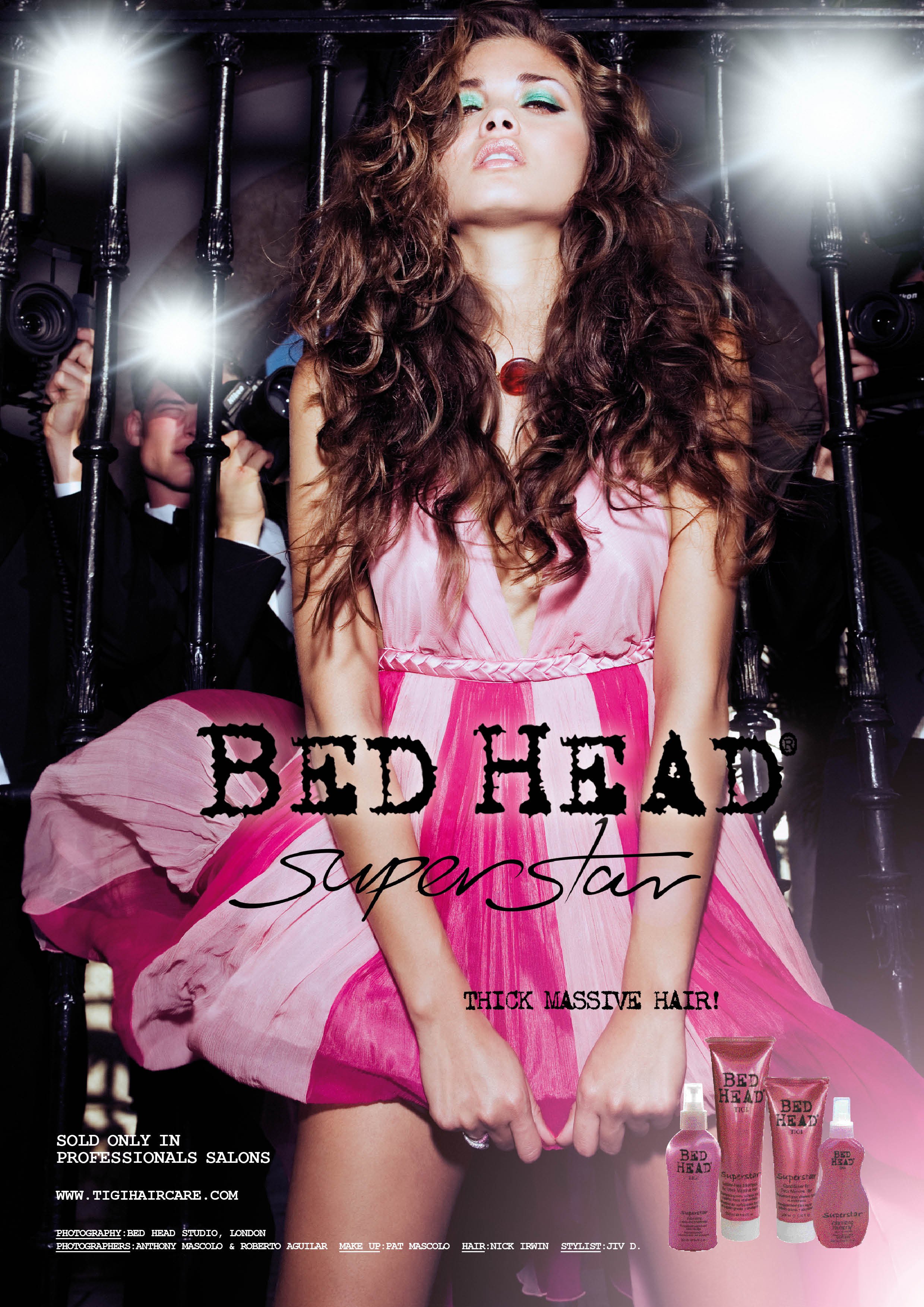 A woman with thick, curly hair wearing a pink dress with her eyes closed, behind metal bars, with photographers taking pictures of her. Text on the image reads 'Redhead Superstar' and promotes hair care products.