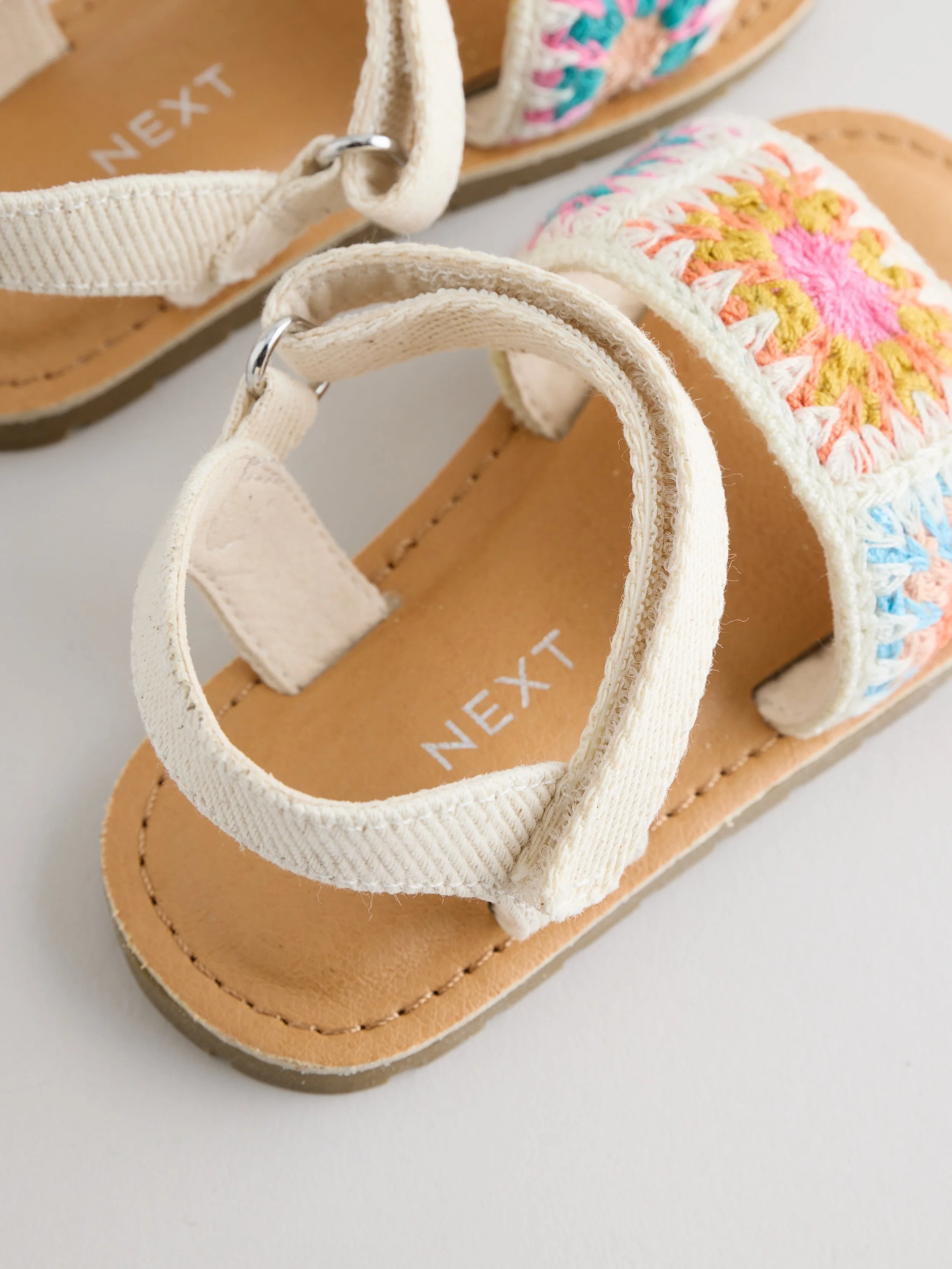 Close-up of a pair of beige sandals with woven straps, placed on a white surface.