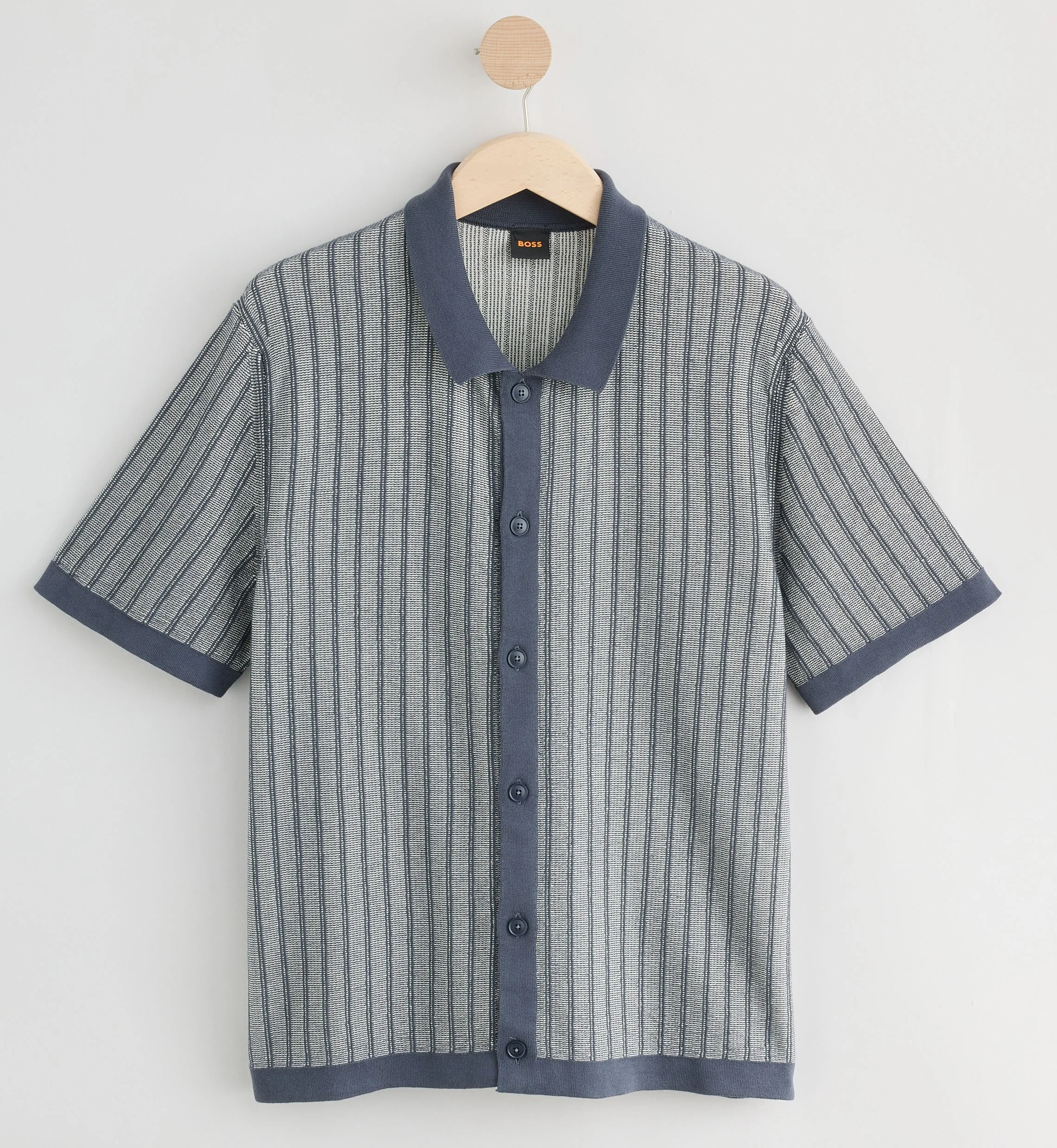 A short-sleeved, button-up shirt with a striped pattern hanging on a wooden hanger against a plain white background.