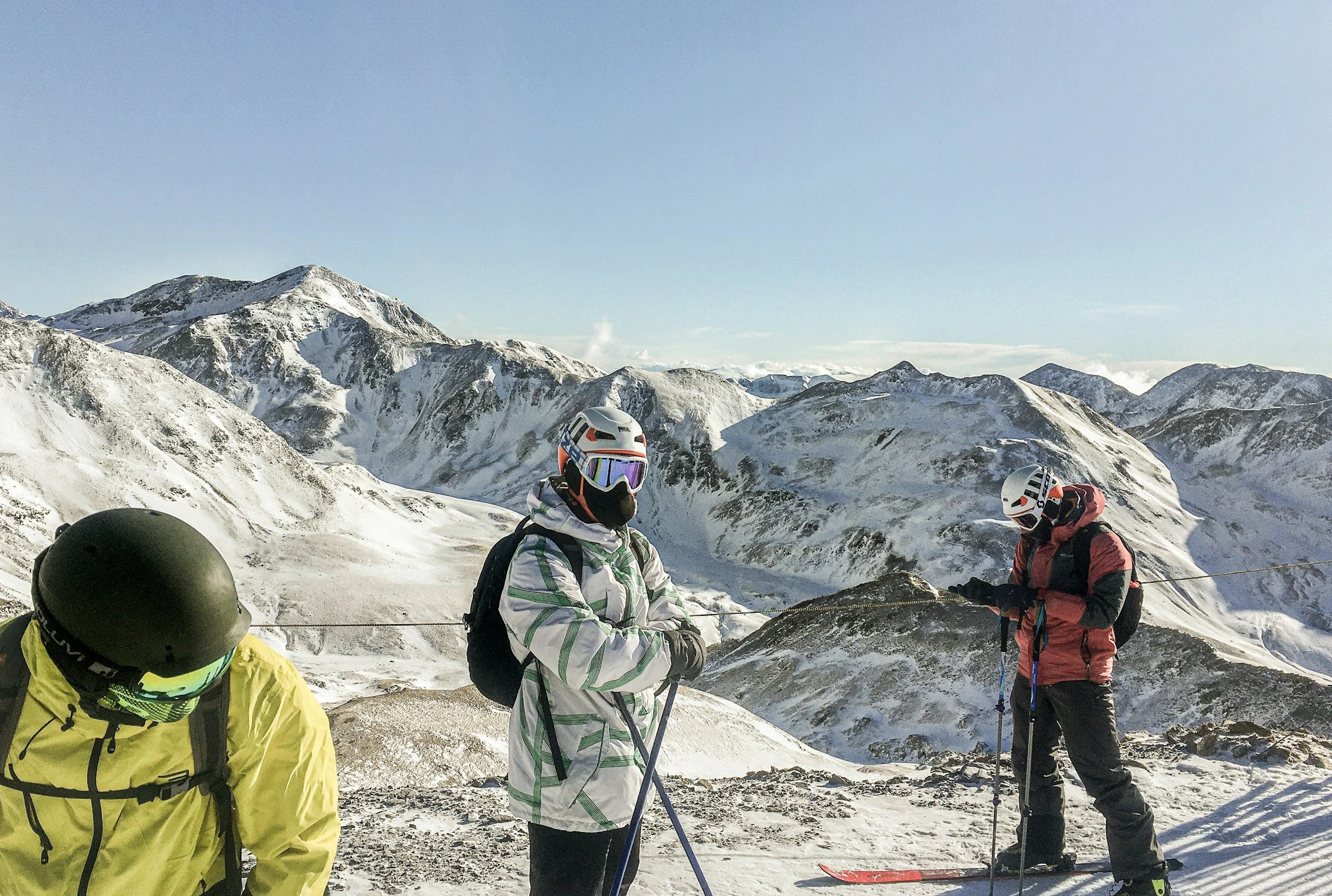 Group of skiers on a snowy mountain slope during daytime with snow-covered mountains in the background.