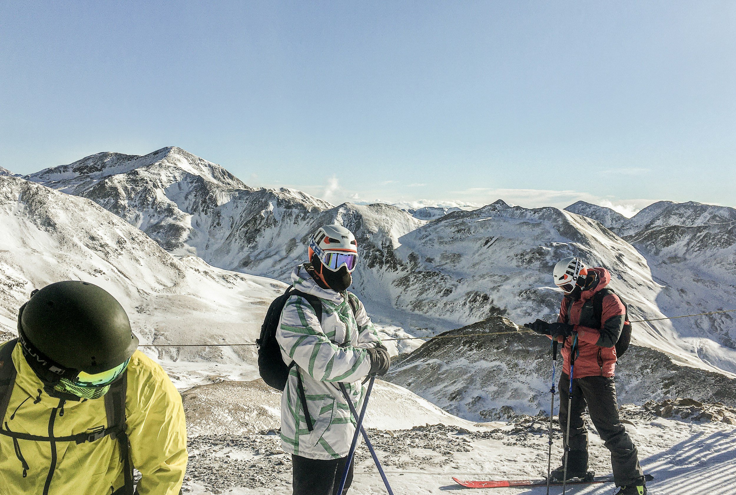 Group of four skiers in winter gear on a snowy mountain with peaks in the background.