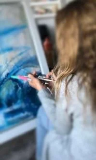 Child using a paintbrush to paint a scenery on an ice surface outdoors.